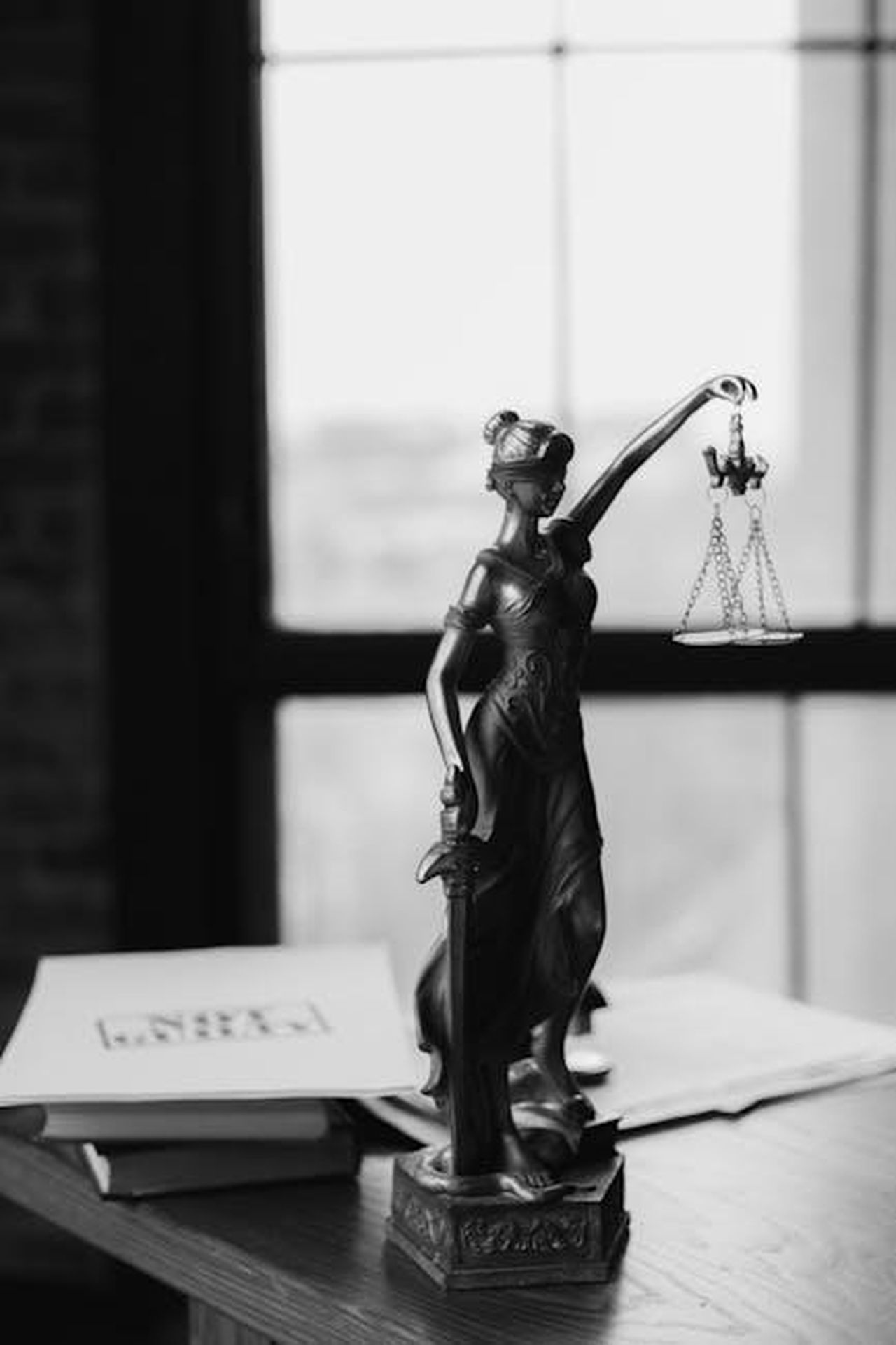 Porsha_Afferma_che_la_Verit_Sar_Rivelata_jMb4QgdtJE - Confidenze24 Source: KATRIN BOLOVTSOVA - pexels - Grayscale photo of Lady Justice statue beside legal documents on a wooden table.