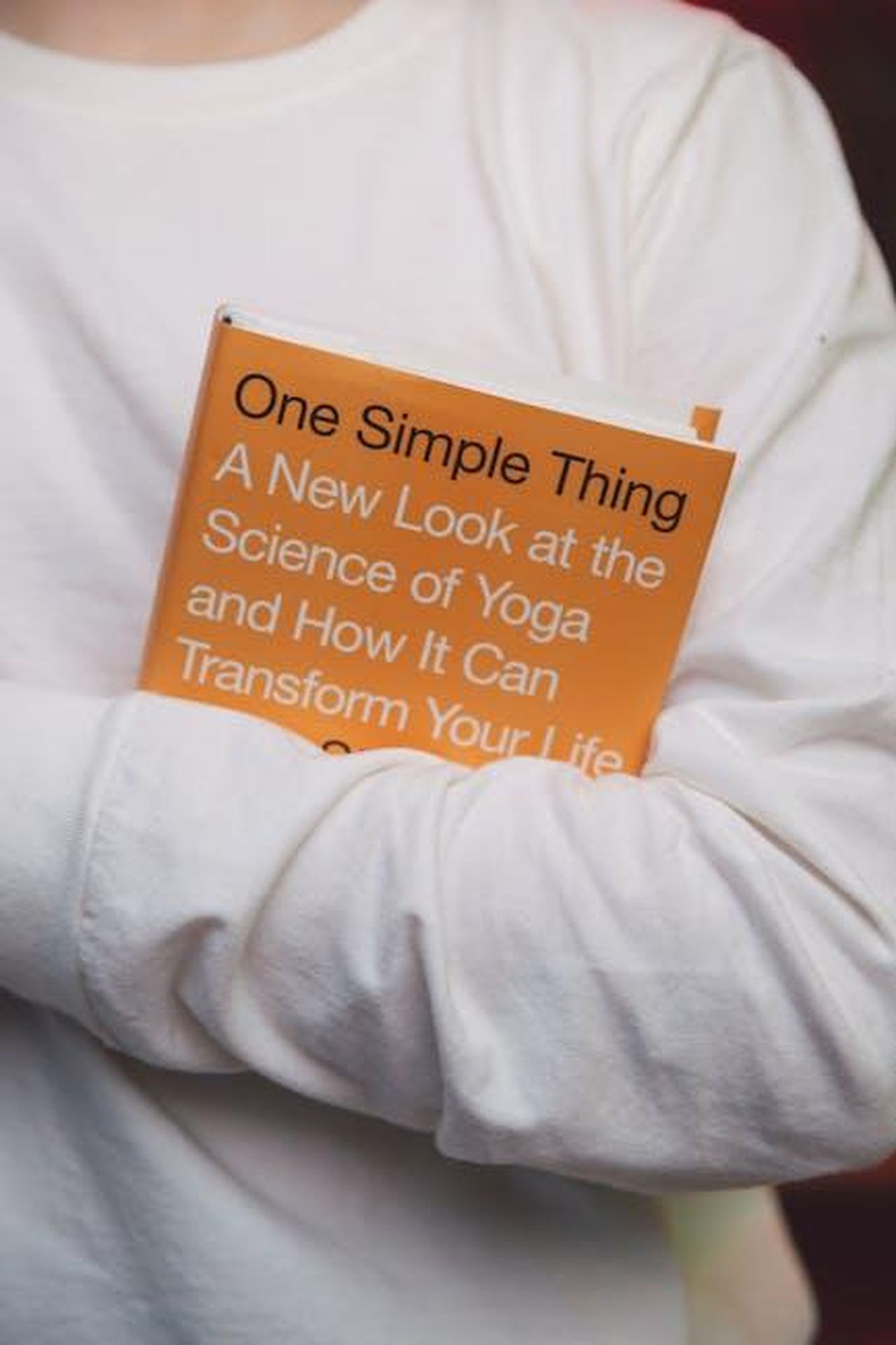 Potrebbe_essere_ritardato_lannuncio_di_ACOTAR_6_LrDY4bpCeW - Confidenze24 Source: Polina Zimmerman - pexels - A person in white holds a yoga book titled 'One Simple Thing.'