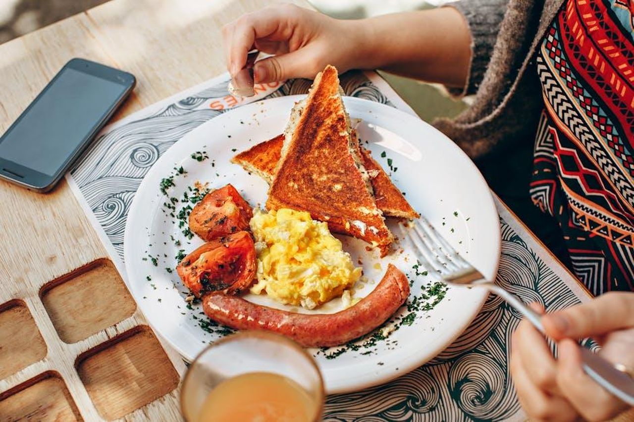 Preparazione_delle_uova_al_pesto_secondo_Symon_xViDXCDXIv - Confidenze24 Source: Helena Lopes - pexels - A cozy brunch scene with toast, scrambled eggs, sausage, and juice.
