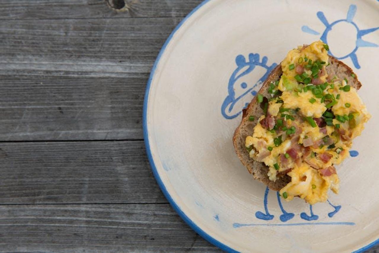 Preparazione_e_risultati_Iduev4K2yP - Confidenze24 Source: Markus Spiske - pexels - Delicious scrambled eggs with ham and chives on toast, served on a whimsical plate.