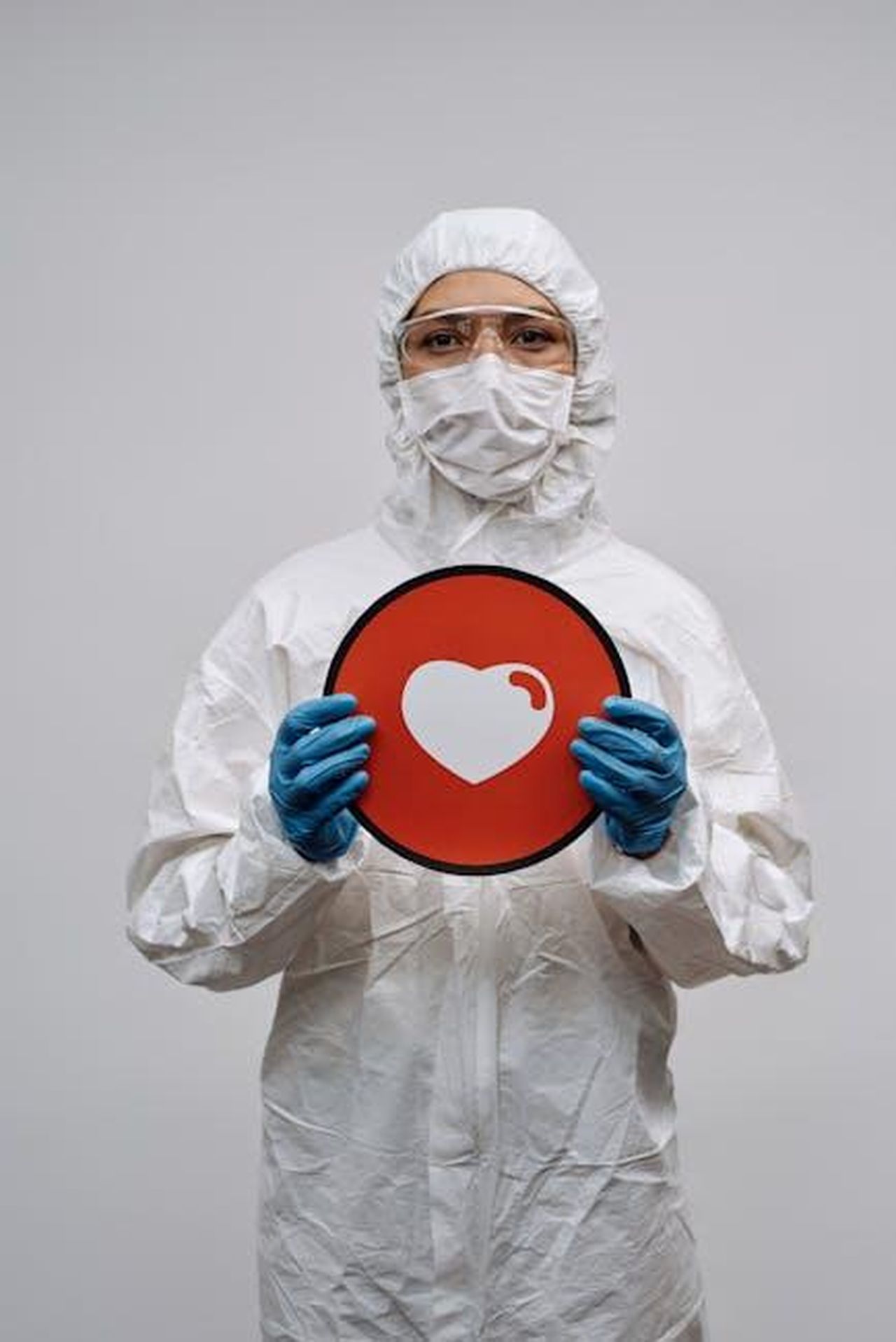Preparazione_per_future_pandemie_S4RJ3ArgGv - Confidenze24 Source: Michelangelo Buonarroti - pexels - Person in PPE holds a heart symbol sign, emphasizing health safety on a white background.