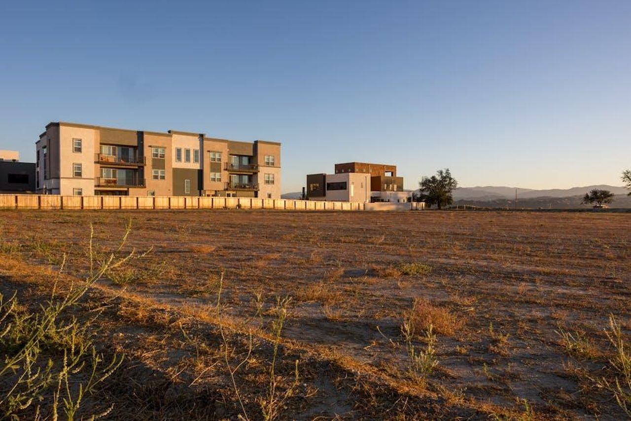 Progetti_futuri_e_nuove_avventure_YJjZwwM4Sq - Confidenze24 Source: David Brown - pexels - Contemporary apartment blocks with ample open field space, framed by distant mountains under a clear blue sky.