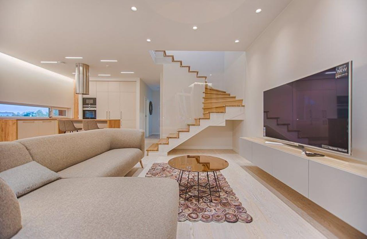 Quali_sono_gli_ascolti_di_The_Way_Home_Stagione_3_8A0EKno1Ye - Confidenze24 Source: Vecislavas Popa - pexels - Spacious modern living room featuring stairs, a TV, and sleek furniture design.