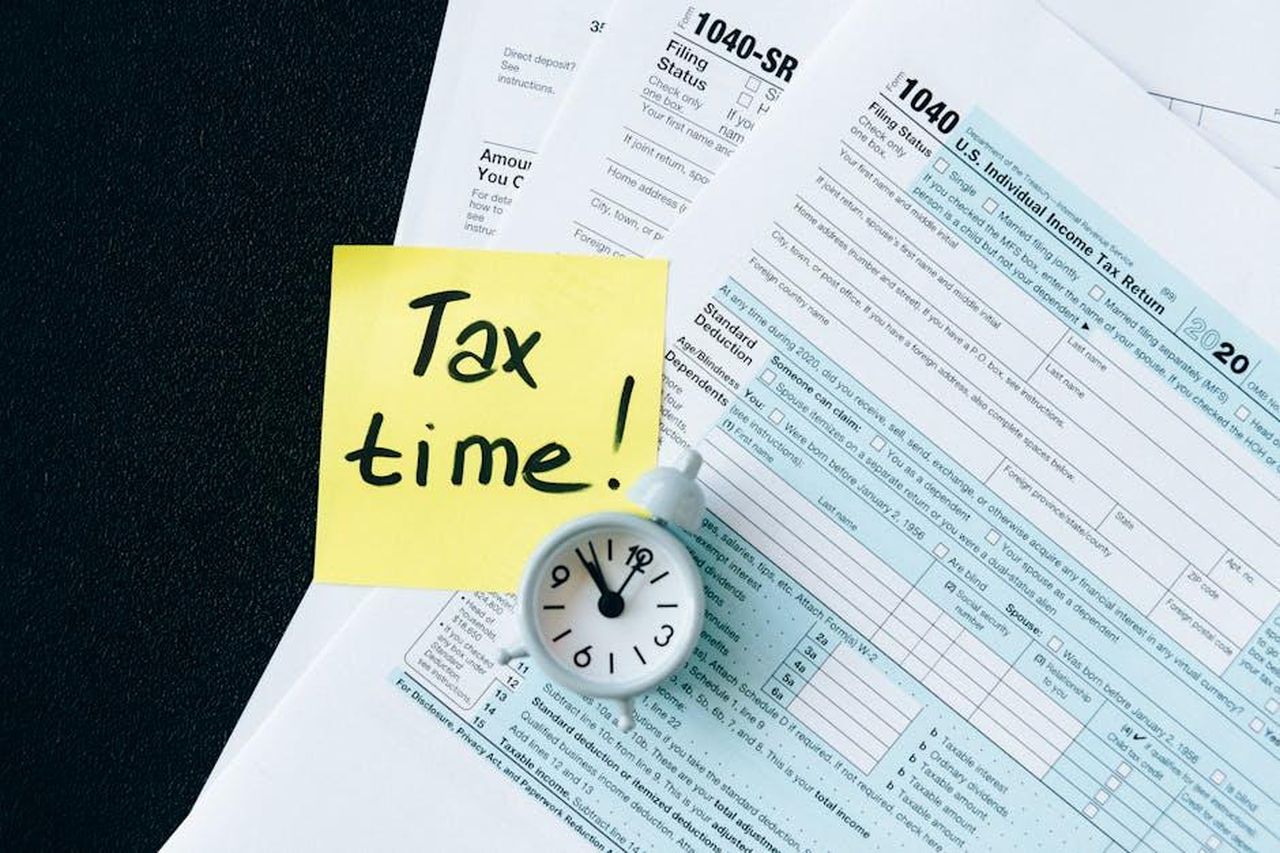 Quando_torner_Vicki_in_EastEnders_UBAyMTheO5 - Confidenze24 Source: Nataliya Vaitkevich - pexels - A stack of tax forms with a clock and yellow sticky note saying 'Tax time!' indicating urgency.