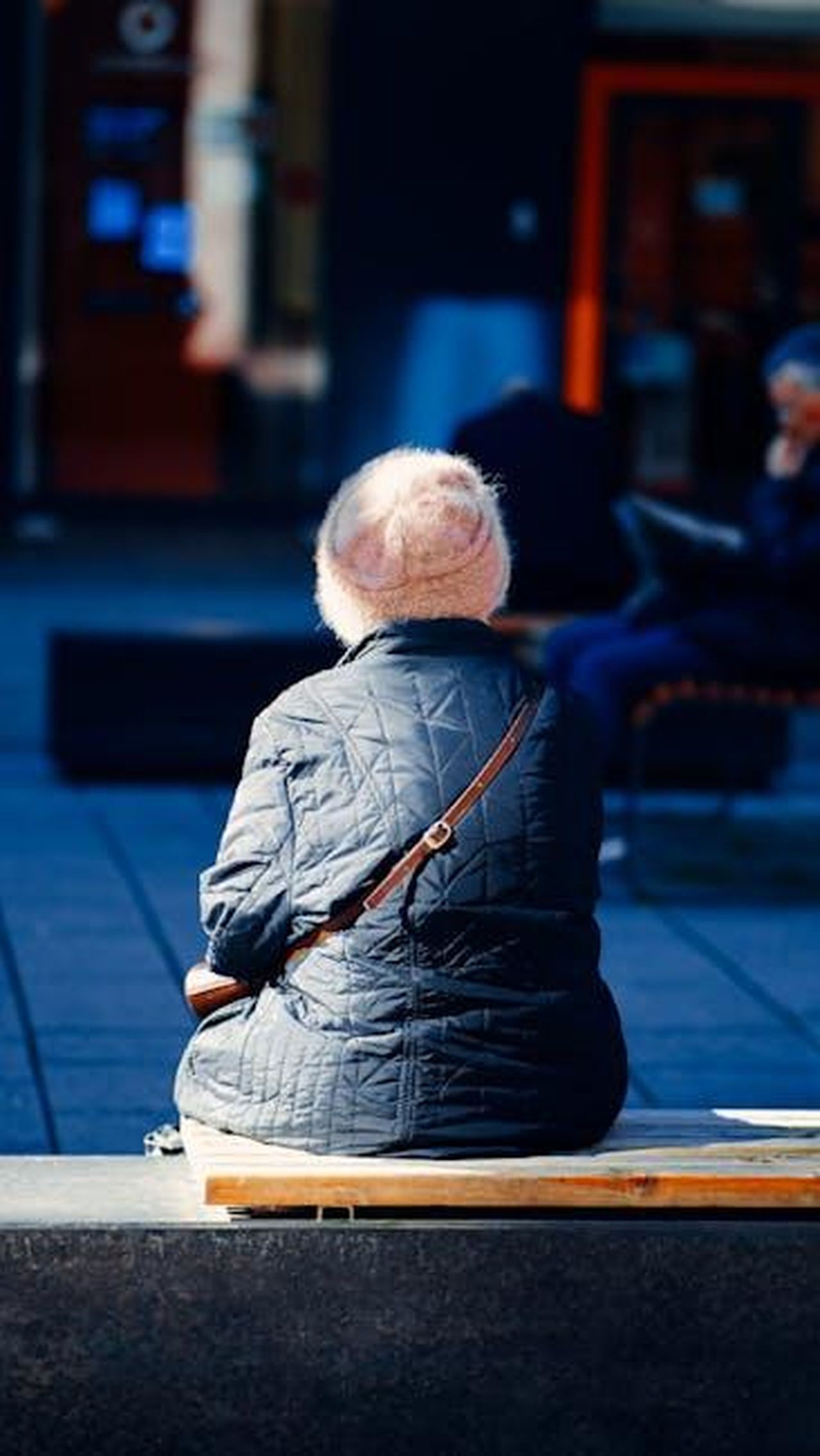 Quanti_anni_ha_Bex_Fowler_QXKFeZbXBn - Confidenze24 Source: Ramon Karolan - pexels - A senior woman in a warm jacket and hat sits on a bench outdoors during a sunny day.