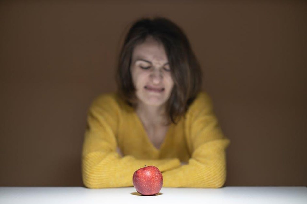 Questo__cos_disgustoso_YQOiV221v3 - Confidenze24 Source: Engin Akyurt - pexels - A woman in a yellow sweater shows disgust while looking at a fresh red apple on a table.