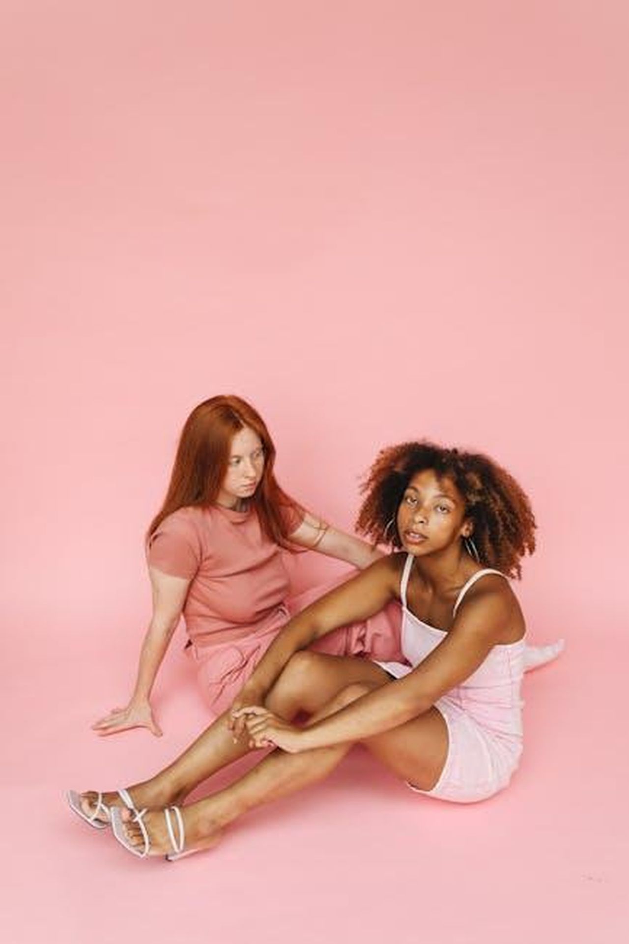 Rachel_e_Russell_volevano_portare_il_dramma_IJrg2l2IuP - Confidenze24 Source: Polina Tankilevitch - pexels - Two young women sitting in a minimalist pink studio portrait showcasing diversity.