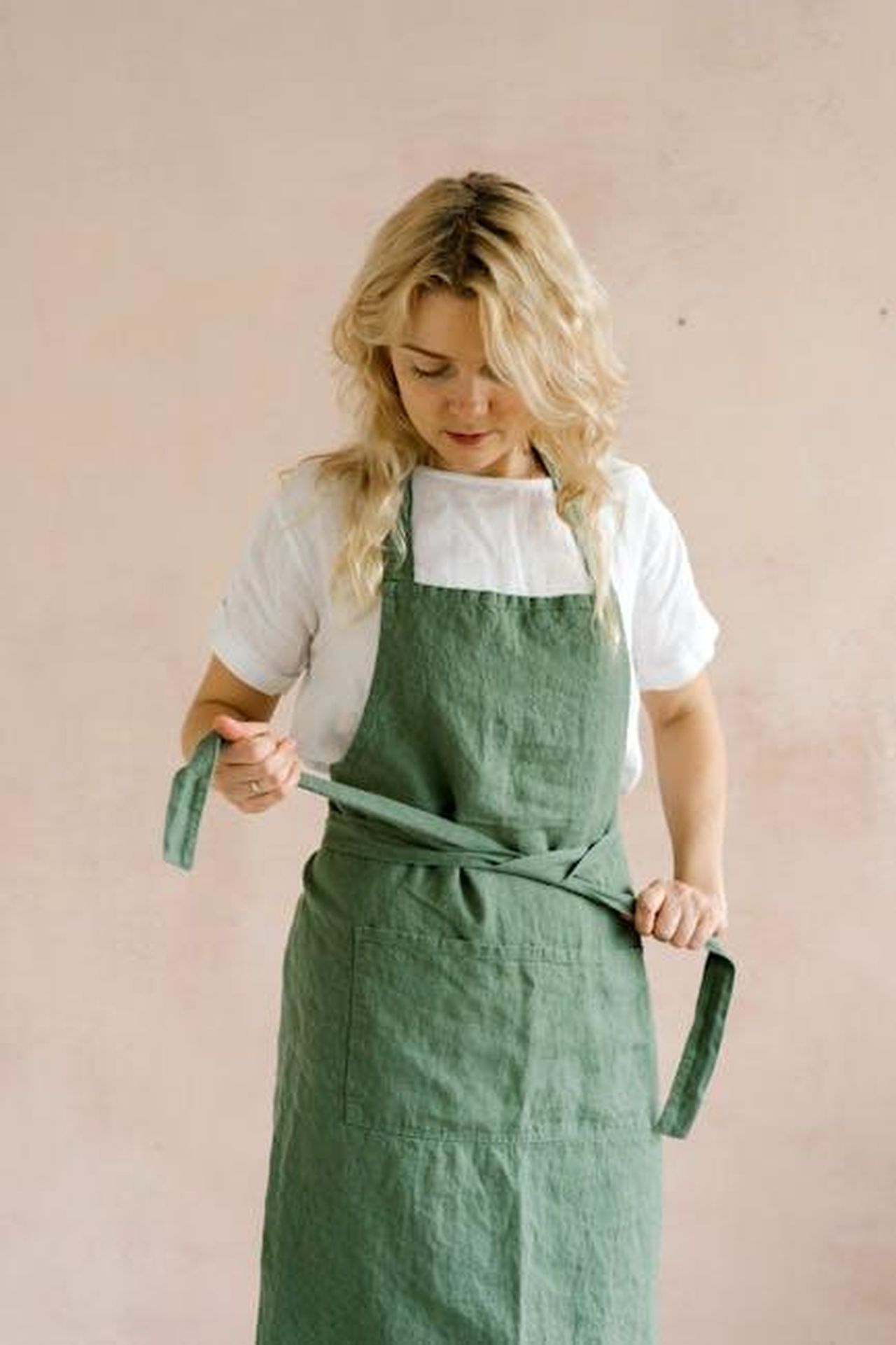 Rapid_Egg_Cooker_PEEPS_x_Dash_Roe88BLPgl - Confidenze24 Source: Mikhail Nilov - pexels - A woman in a green apron adjusts it, standing against a neutral background indoors.
