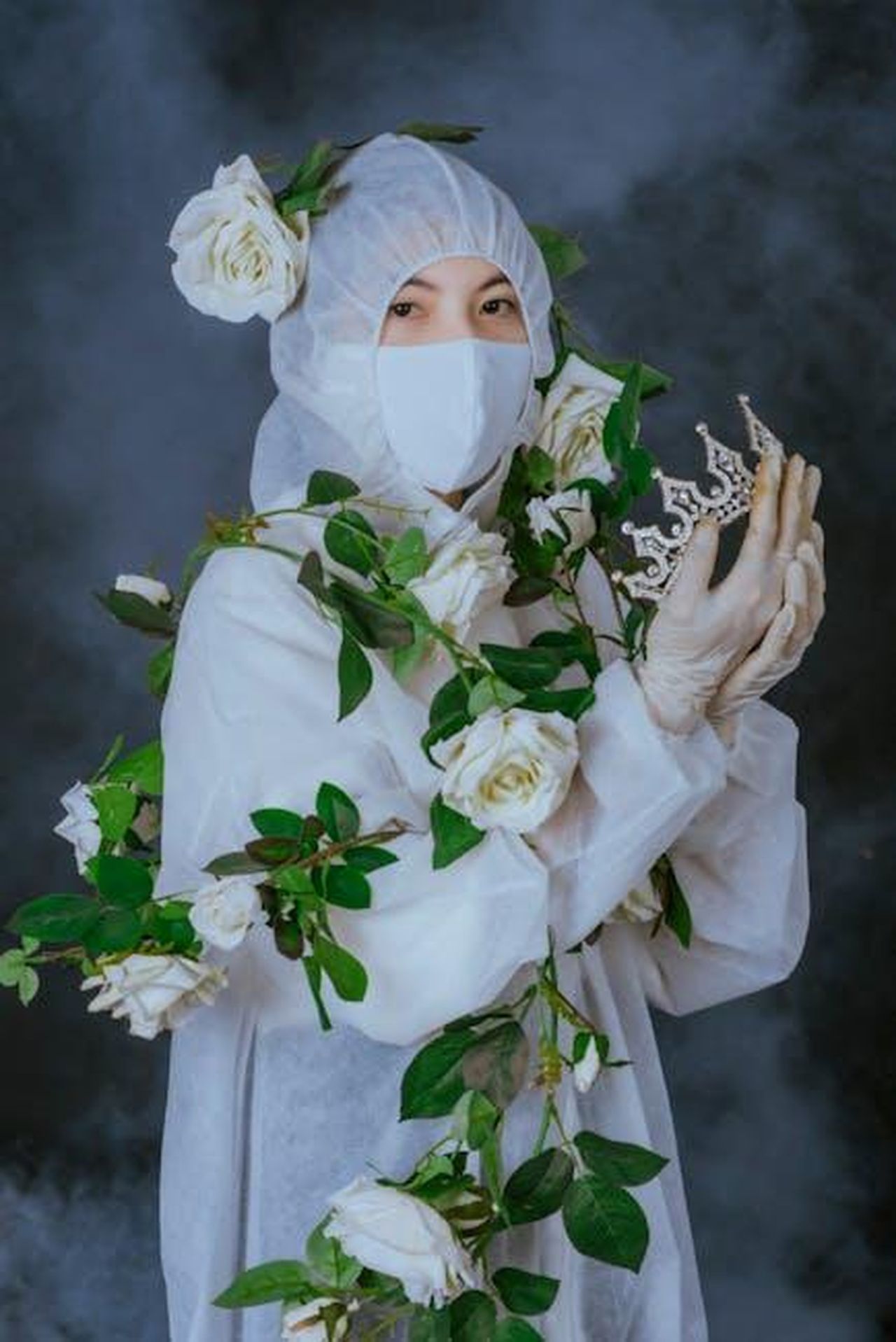 Re_Carlo_III_rompe_il_silenzio_sulla_sua_diagnosi_di_cancro_nCx5KoUqPF - Confidenze24 Source: Nguyễn Văn Minh Vương - pexels - A woman in a hazmat suit holding a crown, surrounded by white roses, symbolizing resilience.
