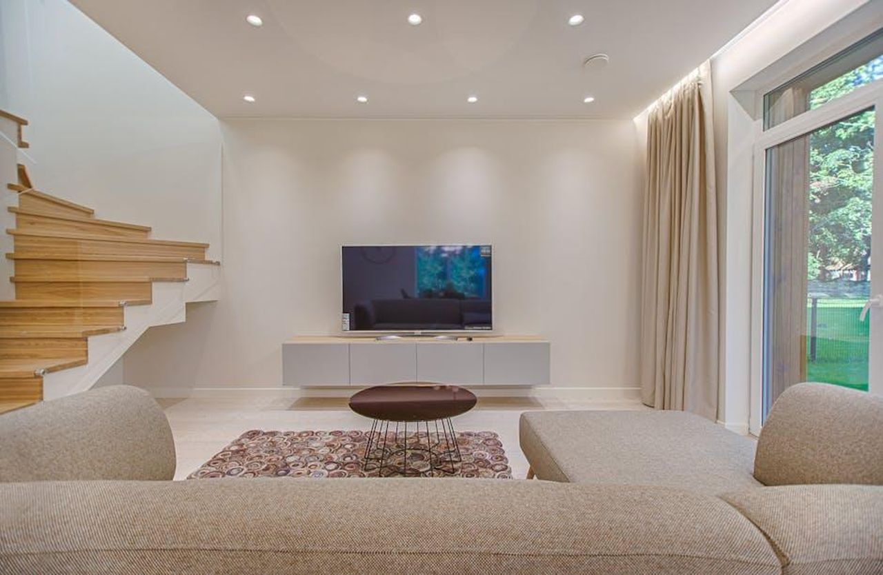 Reazione_allergica_in_diretta_TV_YpkYurXJit - Confidenze24 Source: Vecislavas Popa - pexels - Contemporary living room with stylish sofa, TV, and staircase, offering a cozy interior design setting.