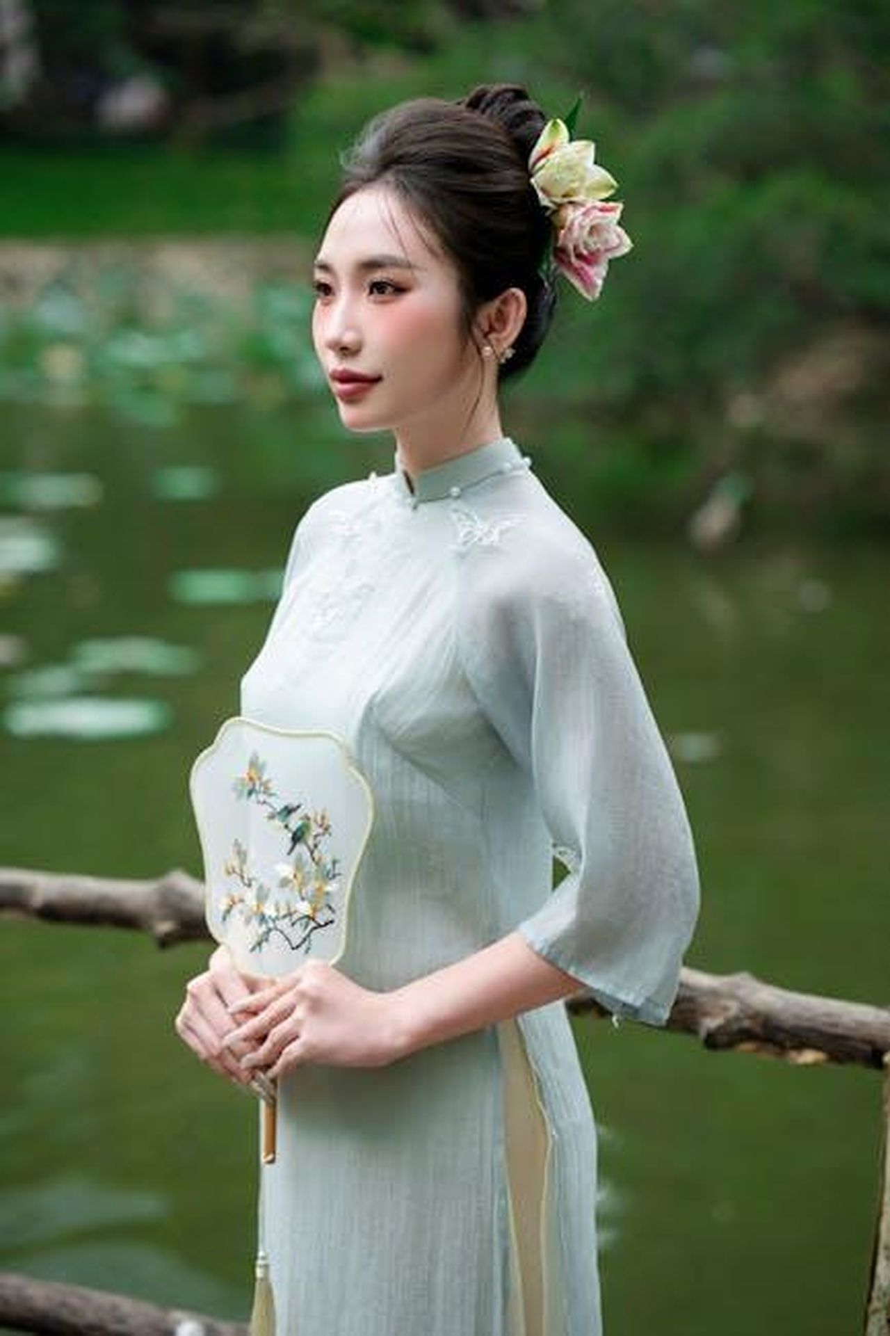 Reazioni_dei_Fan_nOrFX2SISv - Confidenze24 Source: nguyen kha - pexels - A serene portrait of a woman in traditional dress holding a decorative fan by a lakeside.