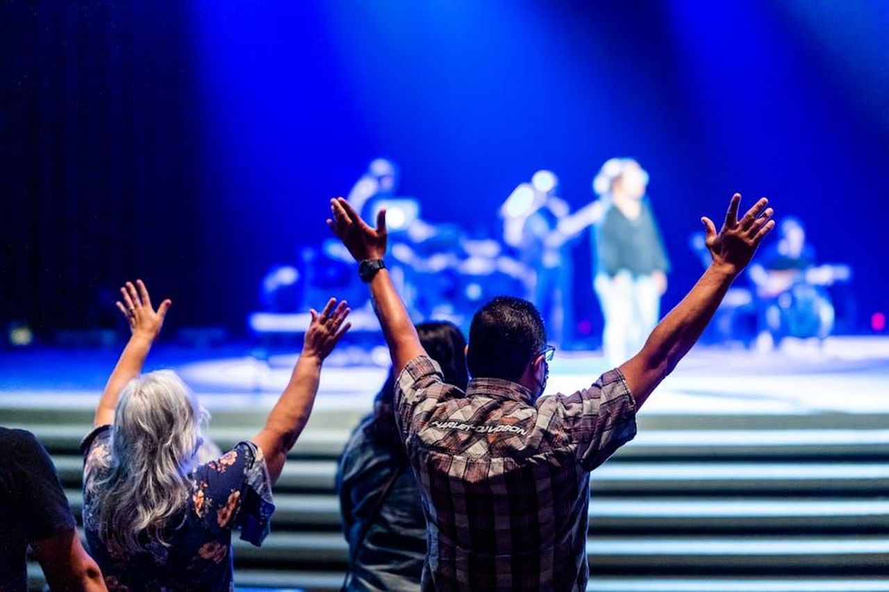 Reazioni_dei_fan_al_tributo_di_Liam_yy8b96hIhP - Confidenze24 Source: Caleb Oquendo - pexels - Excited audience with raised arms watching live music concert on a vibrant blue-lit stage.