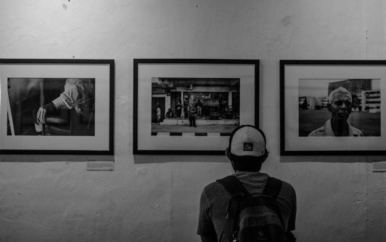 Reazioni_dei_telespettatori_di_A_Place_In_The_Sun_m0sbXaaIQo - Confidenze24 Source: Muhammad Khairul Iddin Adnan - pexels - A man in a cap and backpack admires monochrome art in a gallery.