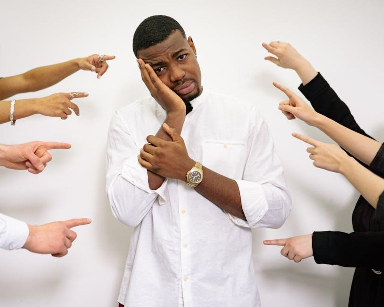 Reazioni_del_Pubblico_alla_Nuova_Canzone_Ejqri2cjrI - Confidenze24 Source: Yan Krukau - pexels - A man in a white shirt looking stressed, surrounded by hands pointing at him.