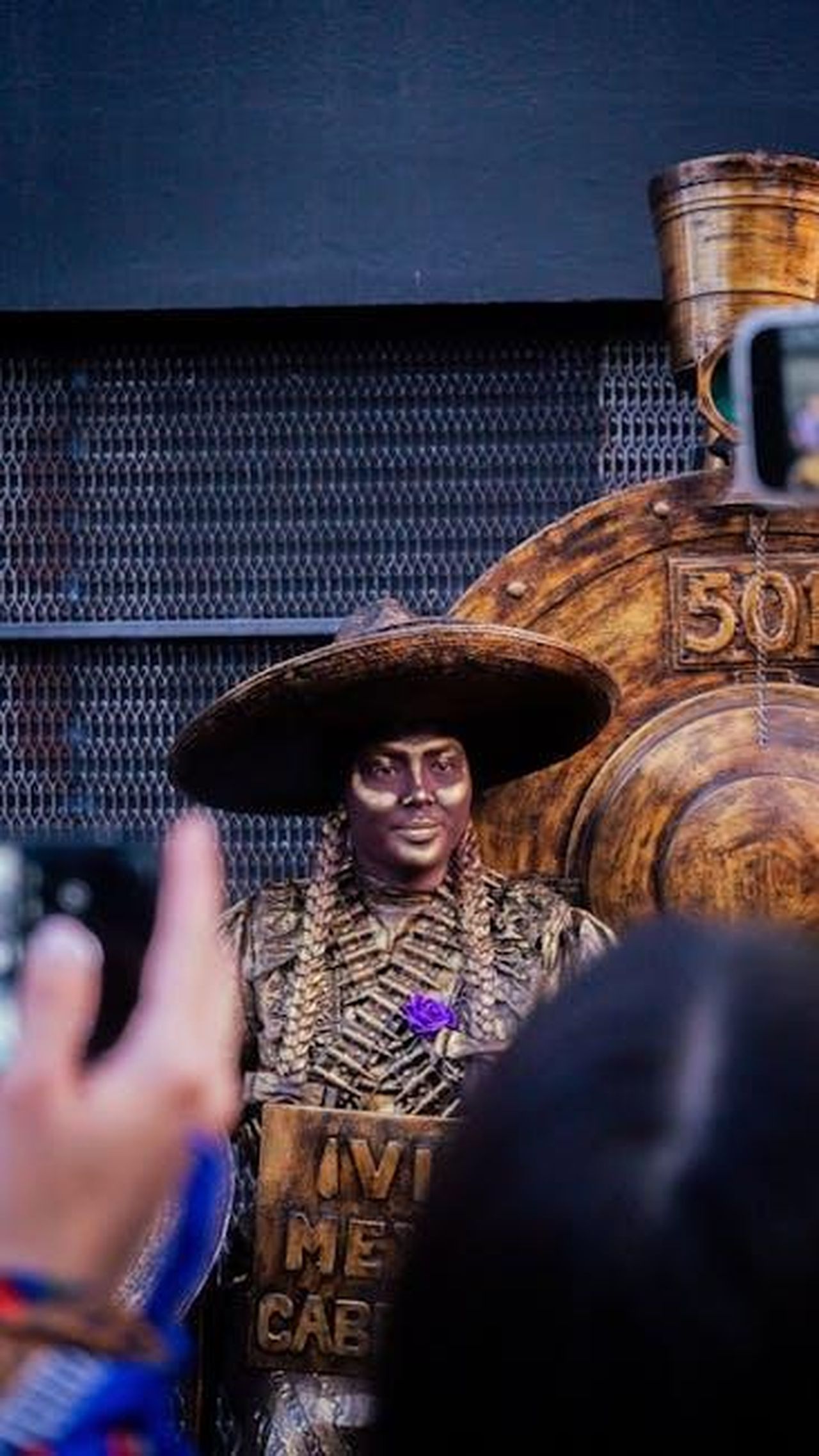 Reazioni_del_pubblico_zpi6n3HC8I - Confidenze24 Source: Sina Rosas - pexels - A street performer dressed in gold costume poses at a vibrant urban festival, captivating the audience.