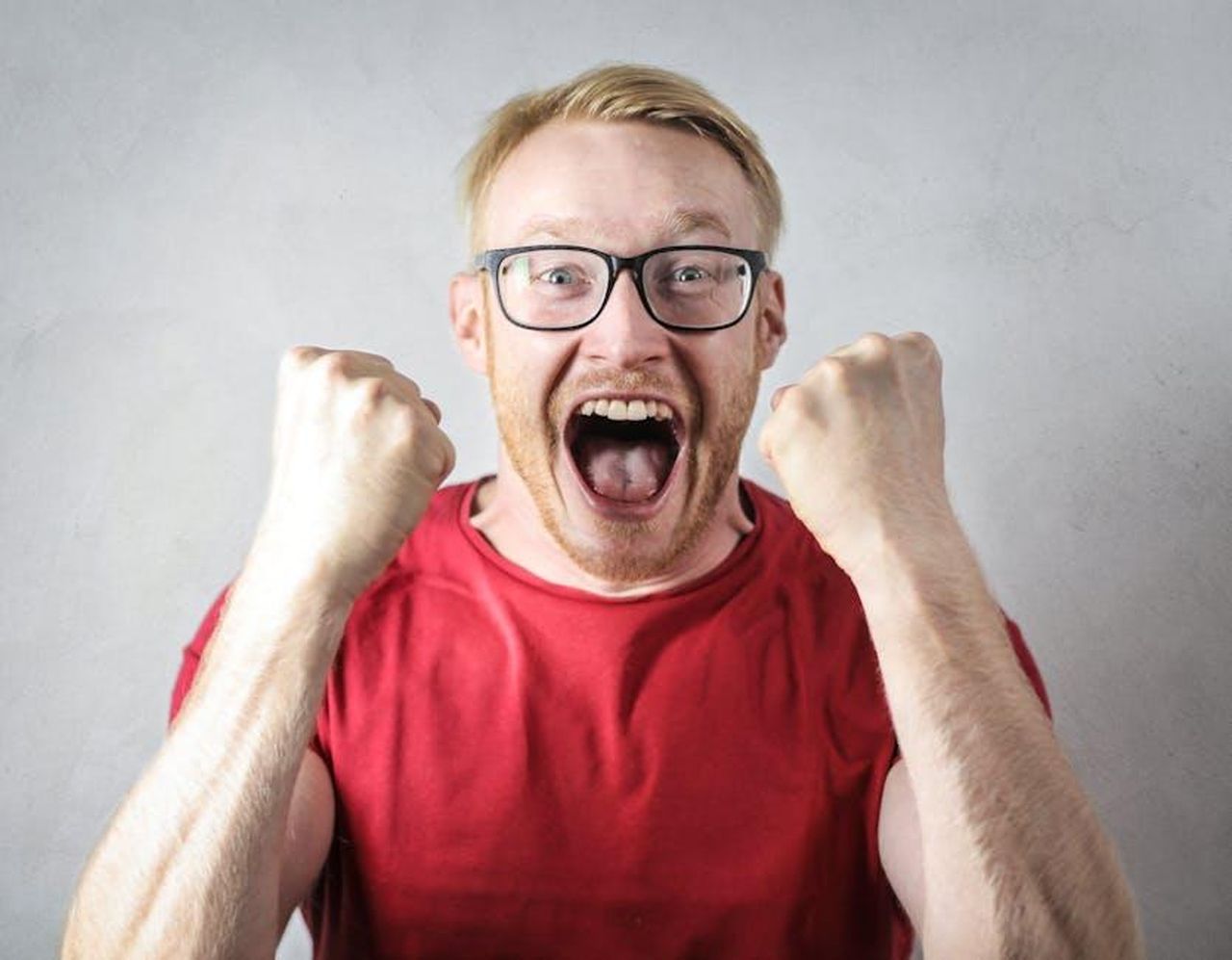 Reazioni_e_commenti_sul_flirt_8MConFDMWw - Confidenze24 Source: Andrea Piacquadio - pexels - A cheerful man in a red shirt expressing excitement indoors.