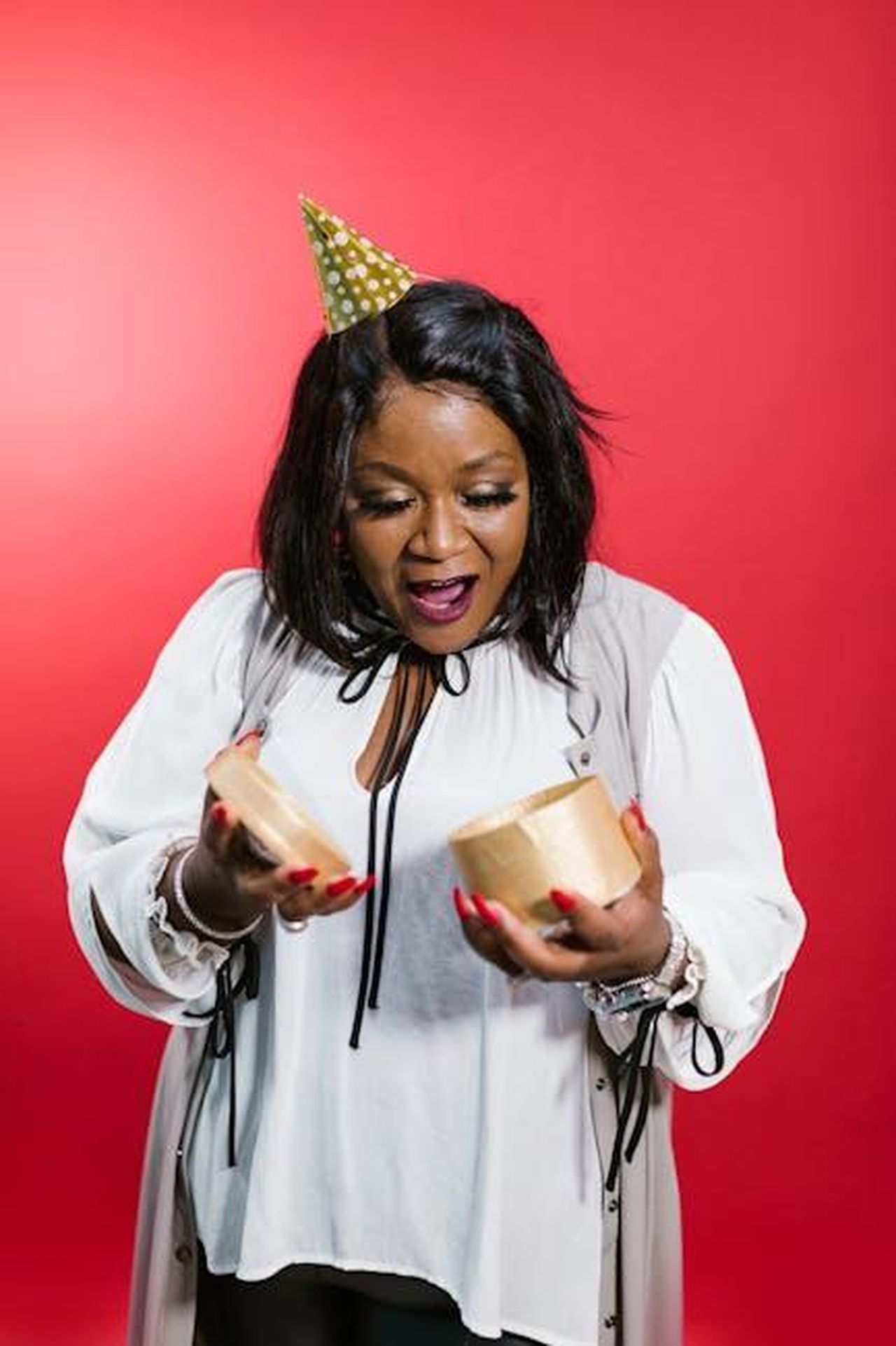 Reazioni_e_commenti_sul_matrimonio_O0eeOTXh3c - Confidenze24 Source: RDNE Stock project - pexels - Delighted woman in party attire unwraps a gift against a vibrant red background.