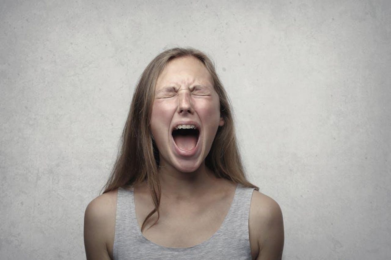 Reazioni_e_dichiarazioni_di_Aaron_Goodwin_QnM5MoI6Re - Confidenze24 Source: Andrea Piacquadio - pexels - Young woman screaming with emotion, showing braces, against a gray backdrop.