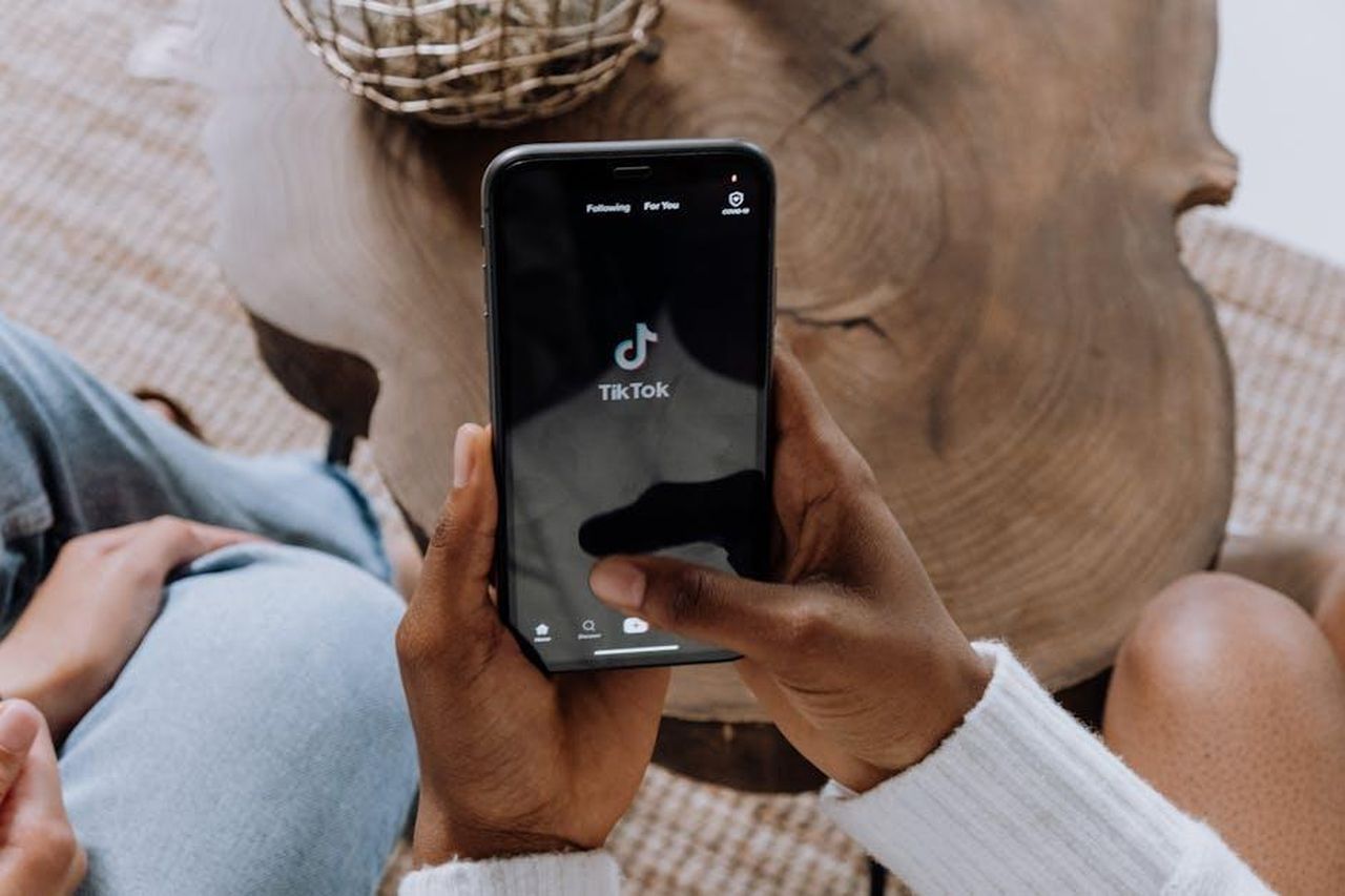 Reazioni_sui_social_media_al_divorzio_di_Quinta_Brunson_0EIKZP44yt - Confidenze24 Source: cottonbro studio - pexels - Close-up of hands holding a smartphone displaying the TikTok app interface on a wooden surface.