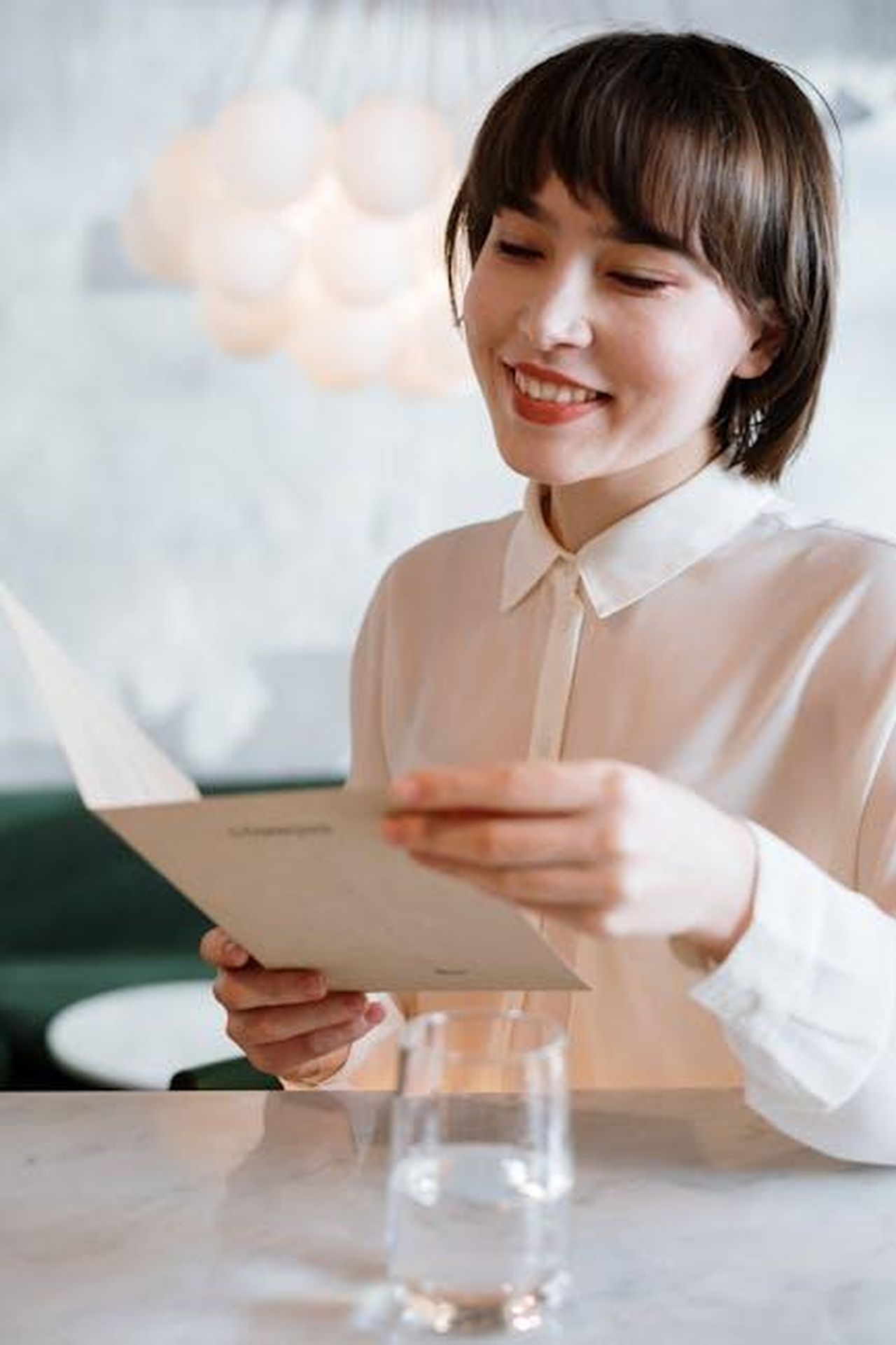 Recensioni_Entusiastiche_degli_Utenti_E4gB4fwGxj - Confidenze24 Source: cottonbro studio - pexels - A smiling young woman in a white shirt reads a menu in a stylish cafe environment.