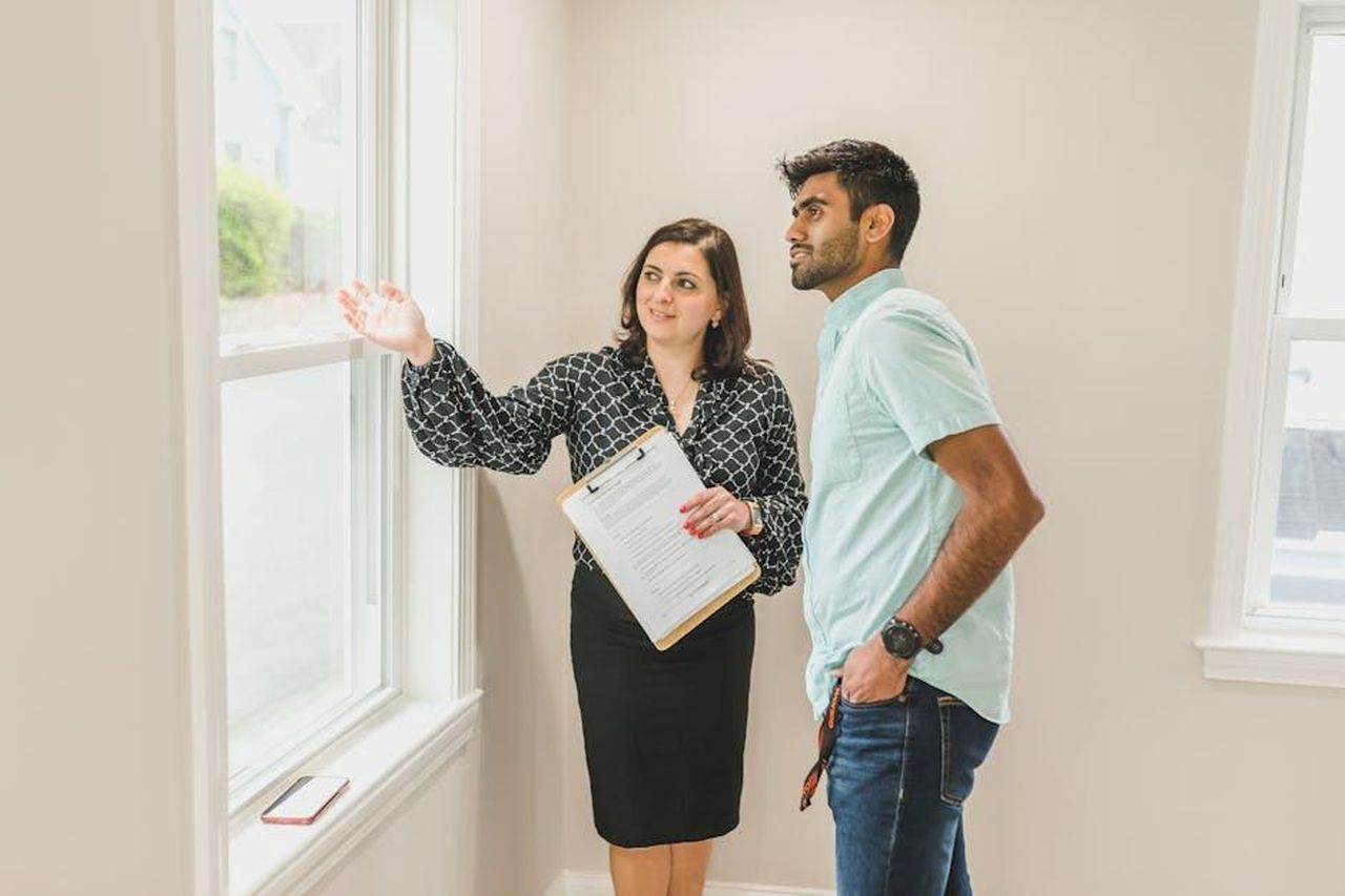 Recensioni_dei_clienti_sui_Pacifica_Sunny_Glow_Bronzing_Drops_sWl9yDhmfZ - Confidenze24 Source: RDNE Stock project - pexels - A real estate agent discusses property details with a client indoors, highlighting the view through large windows.
