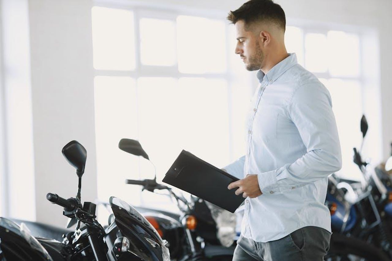 Recensioni_dei_clienti_sul_tappetino_tEf4TQJrEx - Confidenze24 Source: Gustavo Fring - pexels - Man examining motorcycles with a clipboard in a dealership showroom.