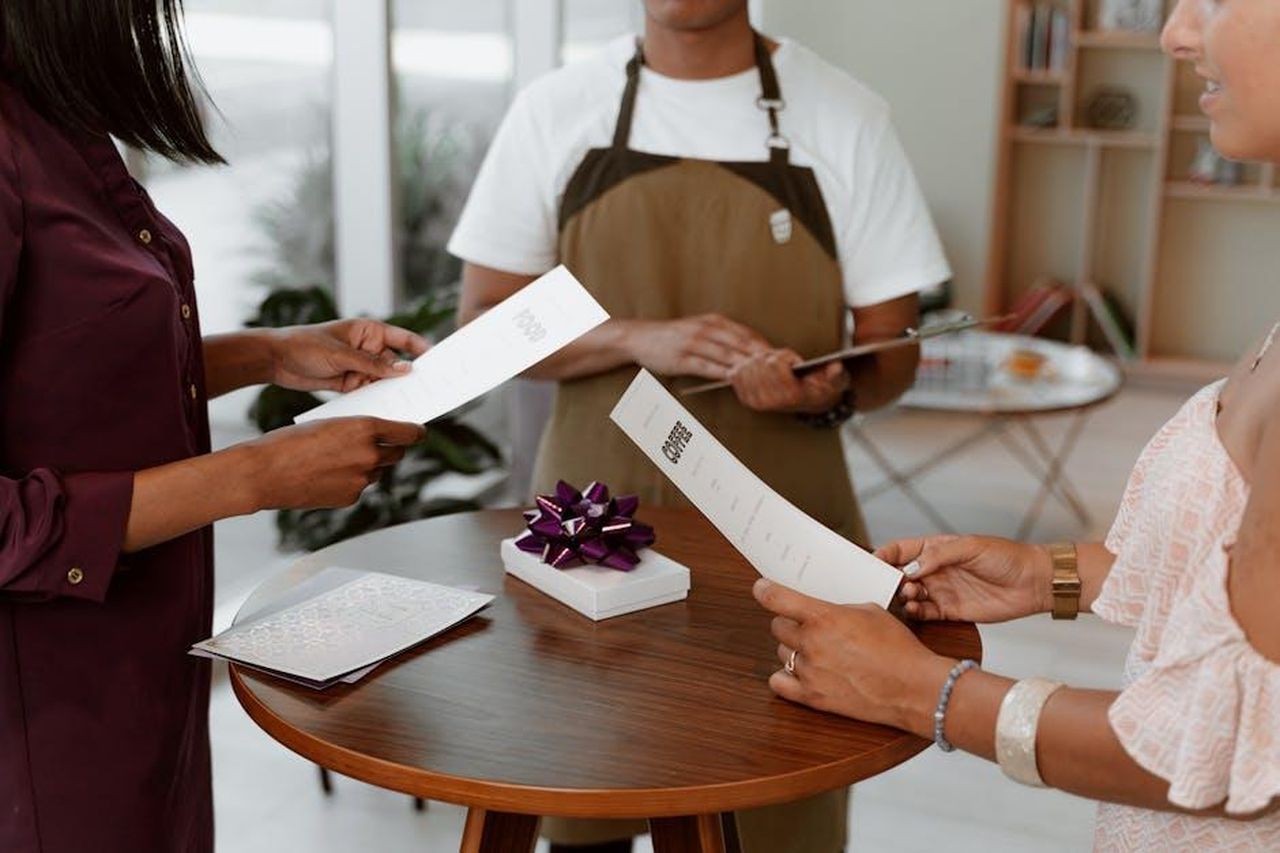 Recensioni_dei_clienti_sulla_collezione_n97CTw1yZI - Confidenze24 Source: RDNE Stock project - pexels - People reviewing a restaurant menu with a gift on a table indoors.