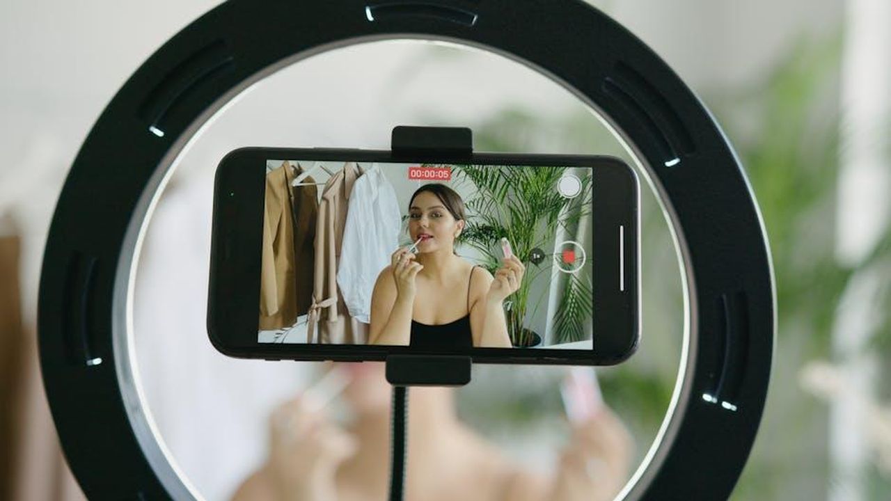 Recensioni_entusiaste_sul_rossetto_harhVKG8T8 - Confidenze24 Source: Anna Nekrashevich - pexels - A beauty vlogger applying lipstick in a vlog recording using a smartphone and ring light.