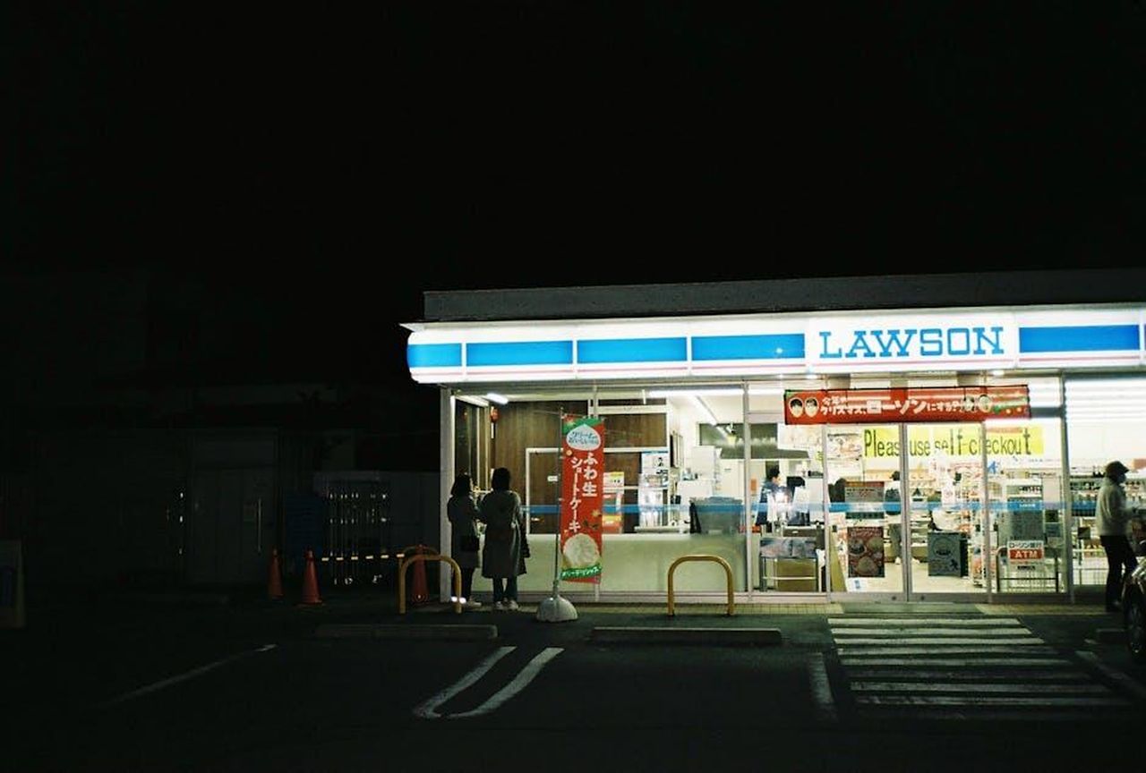Recensioni_entusiastiche_degli_utenti_S9DUF1LjKe - Confidenze24 Source: Benny Analog - pexels - A nighttime view of a Lawson convenience store entrance with people.