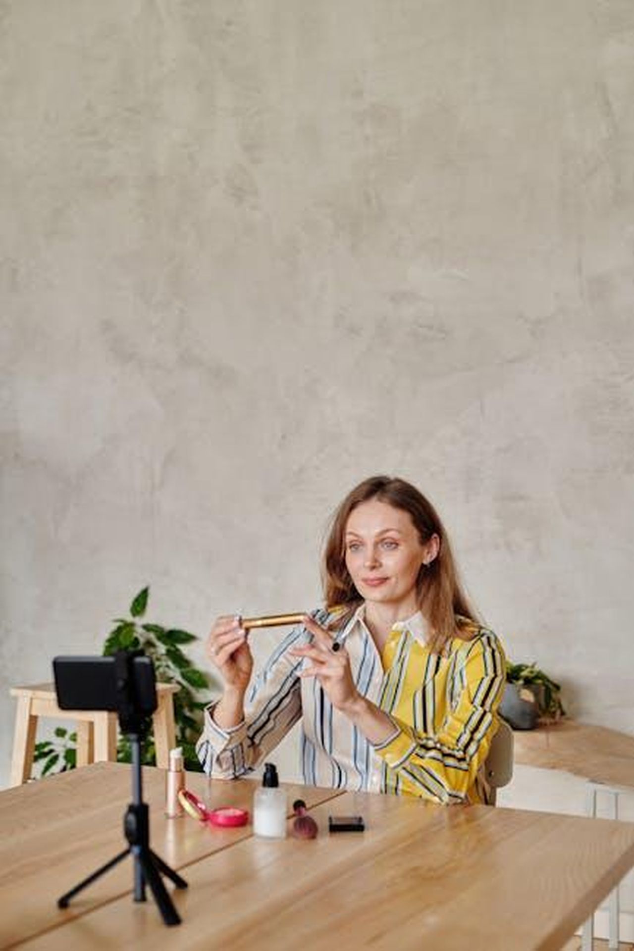 Recensioni_entusiastiche_degli_utenti_qY0bkVFFLT - Confidenze24 Source: Mikael Blomkvist - pexels - Caucasian woman live streaming a beauty vlog, showcasing makeup products on a wooden table.