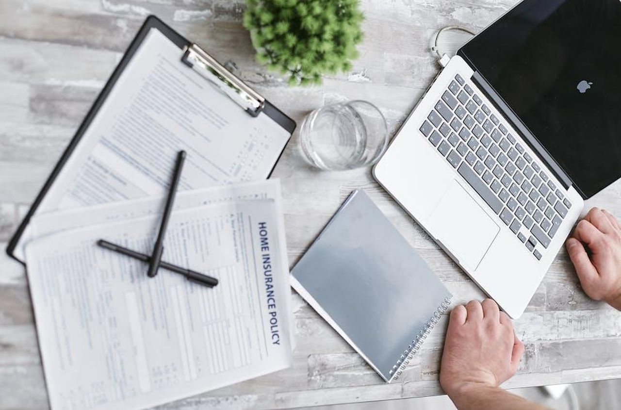 Recensioni_entusiastiche_dei_clienti_CRuwcvSaFh - Confidenze24 Source: Mikhail Nilov - pexels - Top view of home insurance forms, laptop, and documents on a desk, conveying a professional office setting.