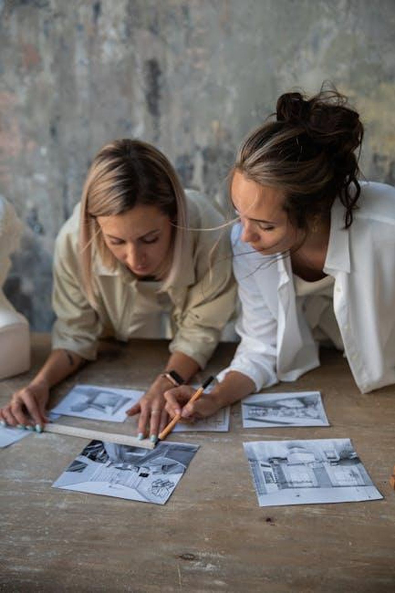 Recensioni_entusiastiche_delle_UGG_Greenport_Slides_PtHyJN5I4U - Confidenze24 Source: KATRIN BOLOVTSOVA - pexels - Two women collaborating over black and white prints on a rustic table.