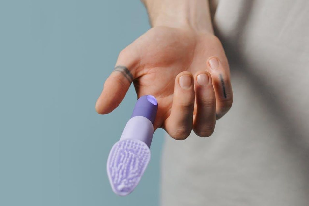 Recensioni_entusiastiche_per_Vibe_HDhWVBihz2 - Confidenze24 Source: cottonbro studio - pexels - A close-up image showing a hand holding a purple silicone finger vibrator against a neutral background.