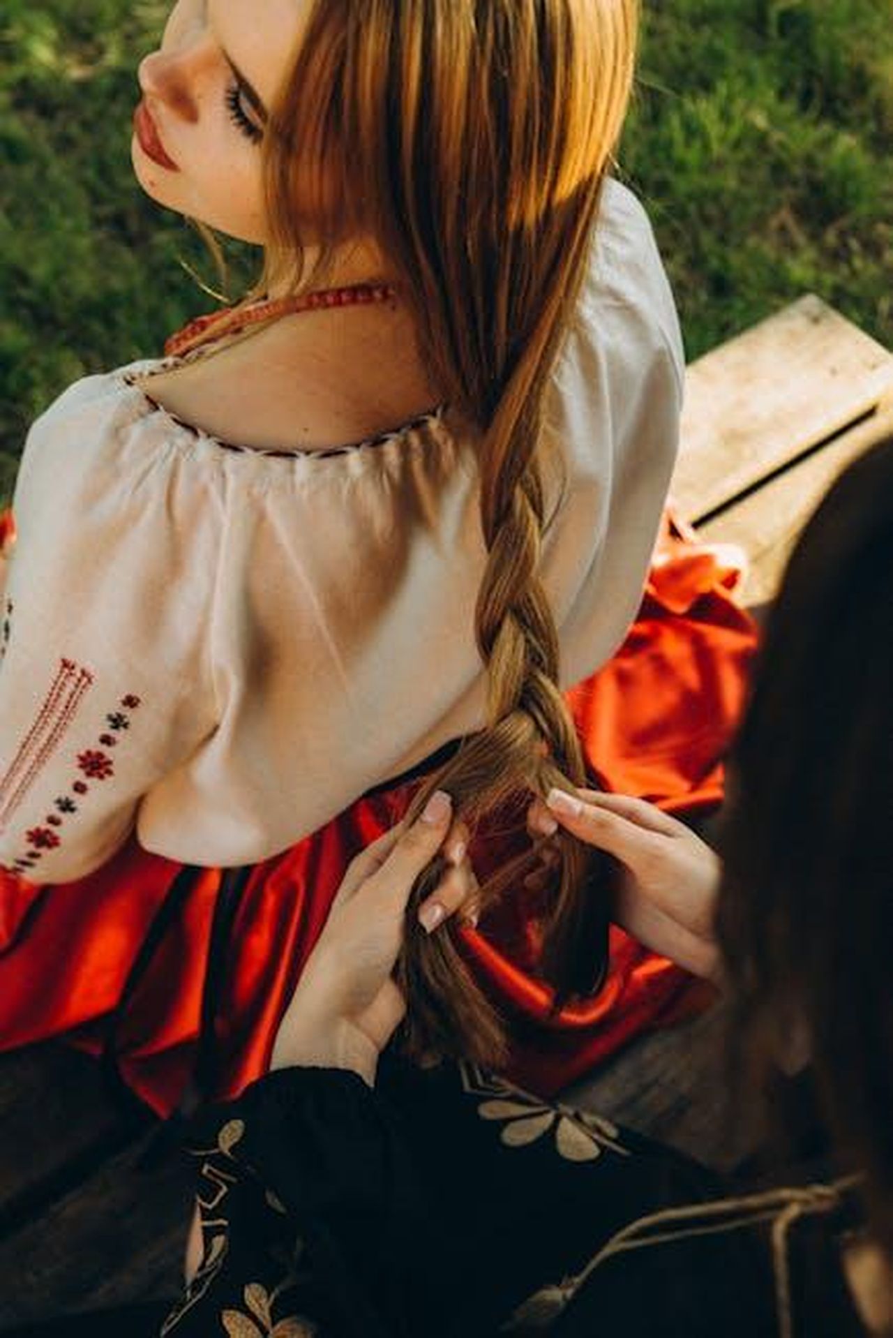 Recensioni_entusiastiche_per_il_Tap_Secret_C4TXuPH19Q - Confidenze24 Source: Ярина Бурштинович - pexels - A woman in traditional attire braiding hair outdoors, showcasing cultural heritage.