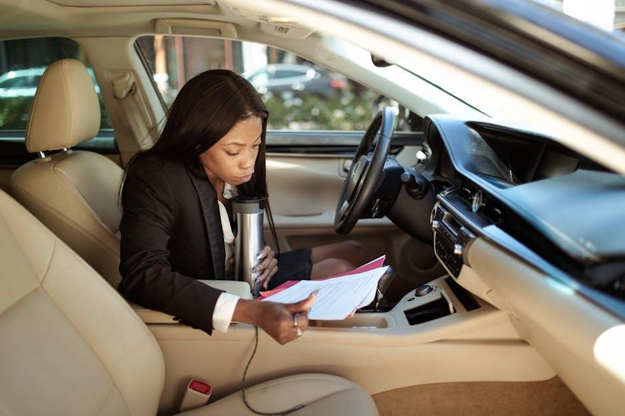Recensioni_entusiastiche_sul_tumbler_Stanley_3tydzNGWg0 - Confidenze24 Source: RDNE Stock project - pexels - A focused businesswoman reads documents in her car, multitasking with a tumbler.