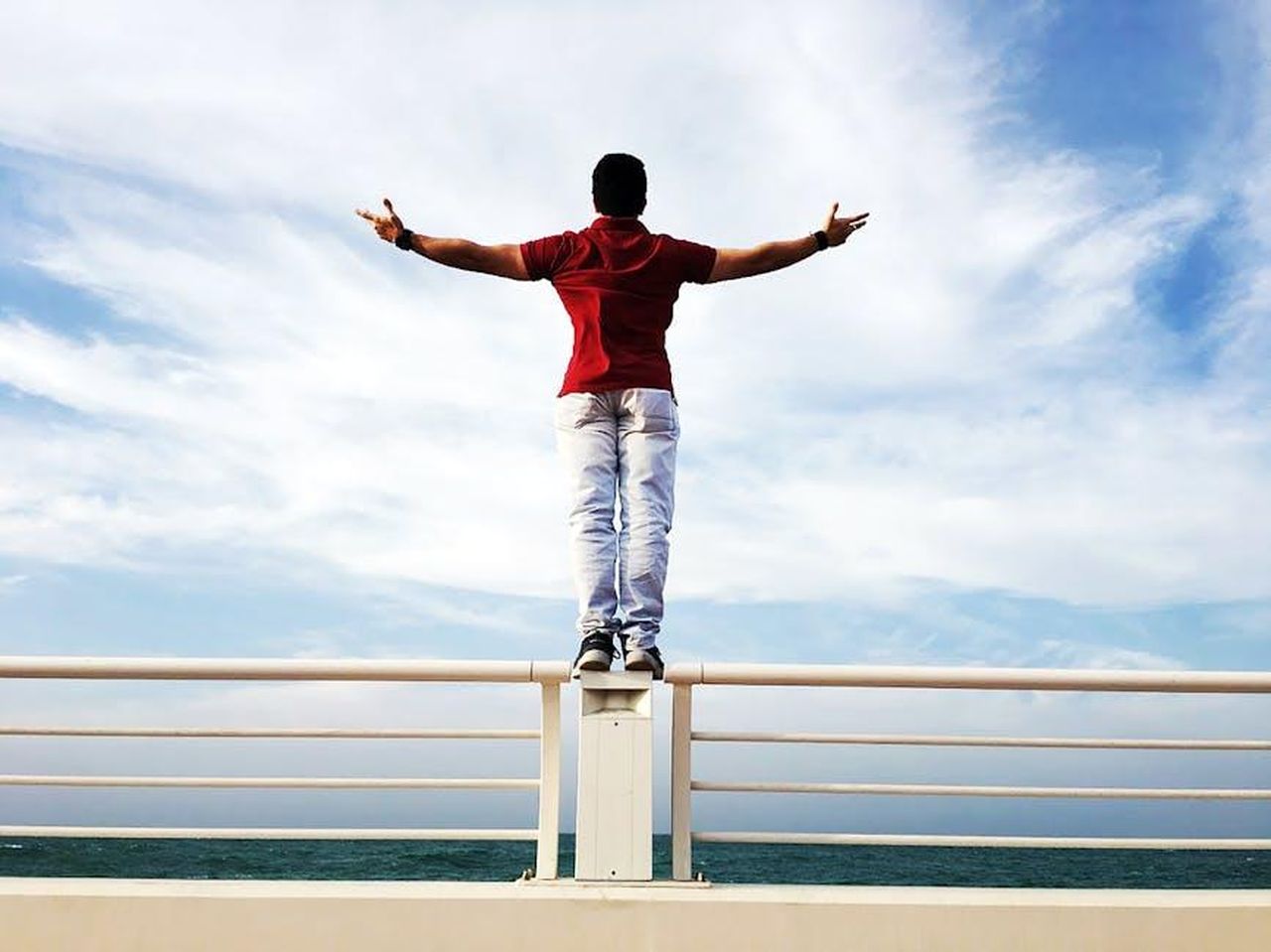 Responsabilit_nel_mondo_reale_w6GA9tUrz2 - Confidenze24 Source: Sanketh Rao - pexels - A person standing on a railing by the sea with arms outstretched under a clear sky, symbolizing freedom.