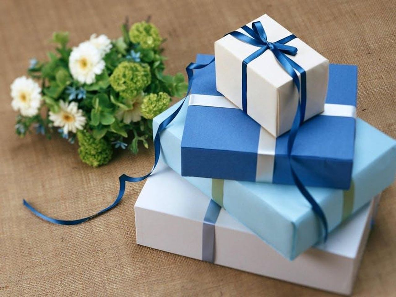 Ricevere_regali_NNKNaAzp1z - Confidenze24 Source: Pixabay - pexels - Three beautifully wrapped gift boxes with blue ribbons arranged beside a floral bouquet.