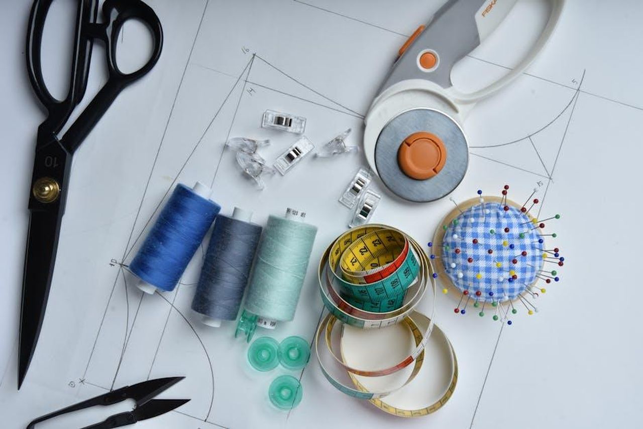 Riflessioni_di_Eva_Mendes_sulla_moda_s5pZ8RVzZM - Confidenze24 Source: Jacob Moseholt - pexels - A collection of sewing tools including scissors, thread, and rotary cutter on pattern paper, perfect for tailoring.