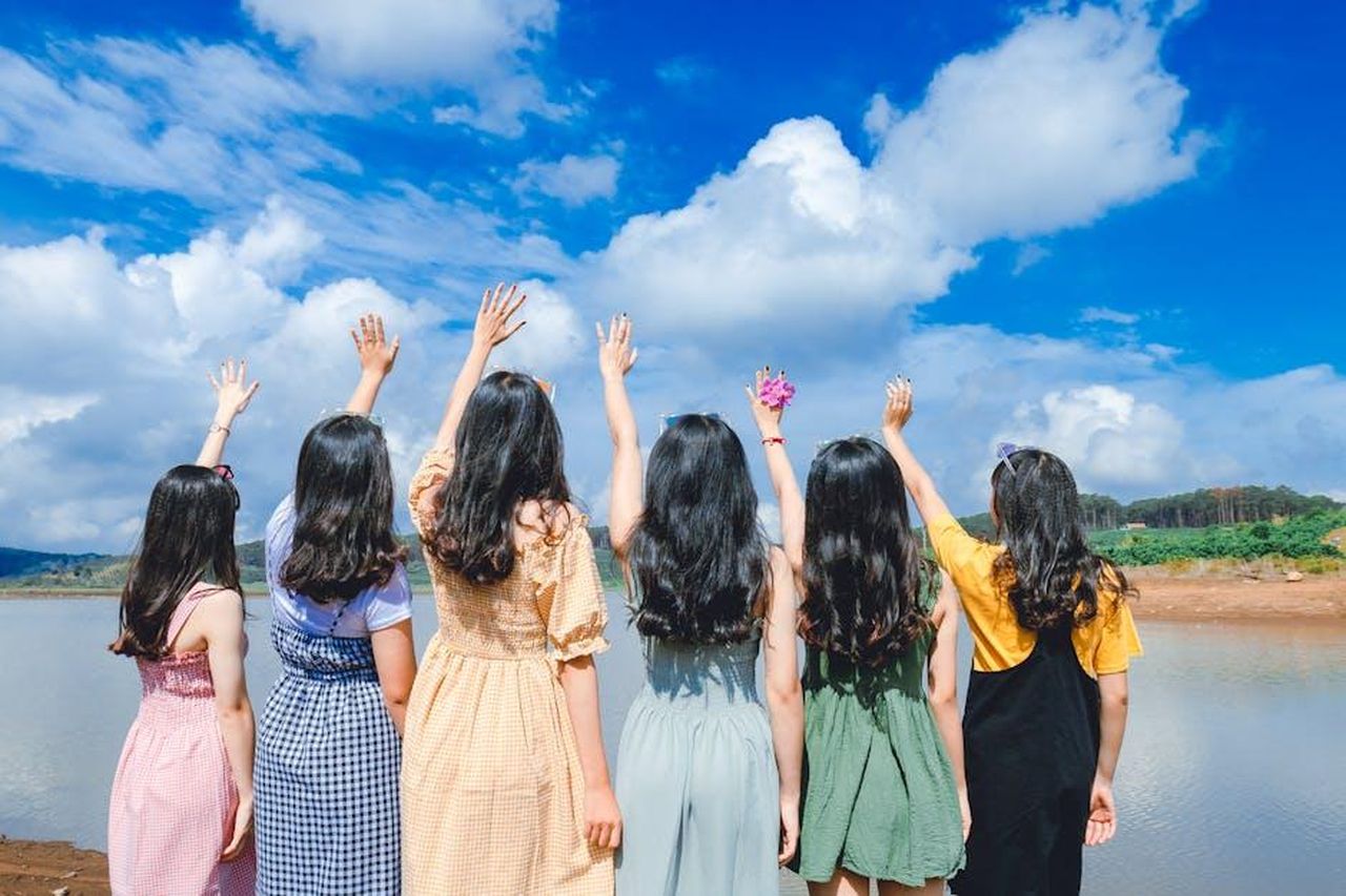 Riflessioni_sulla_carriera_e_lamicizia_PR3Ex2bp8G - Confidenze24 Source: Chu Chup Hinh - pexels - Group of young women with long hair raising hands by a lake under a clear blue sky.