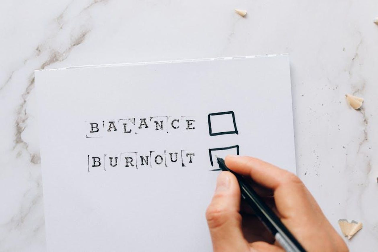 Riflessioni_sulla_sua_carriera_jSo3aNeMvt - Confidenze24 Source: Nataliya Vaitkevich - pexels - Close-up of a hand hovering over a checklist with options for balance or burnout, symbolizing stress and choice.