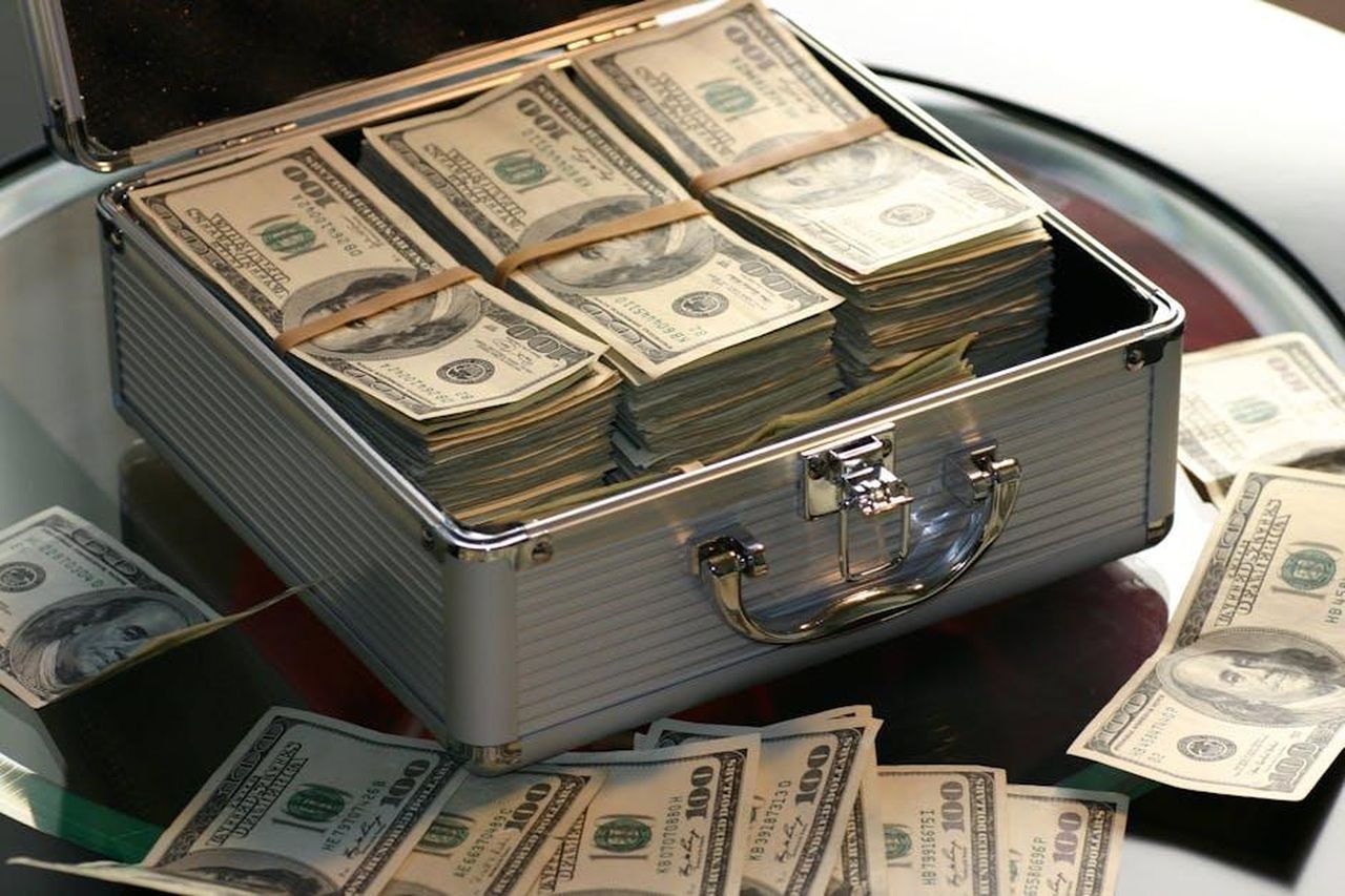 Robert_Herjavec_e_il_suo_successo_finanziario_Lydv1lkTWv - Confidenze24 Source: Pixabay - pexels - Open briefcase filled with stacks of hundred dollar bills on a glass table, representing wealth.