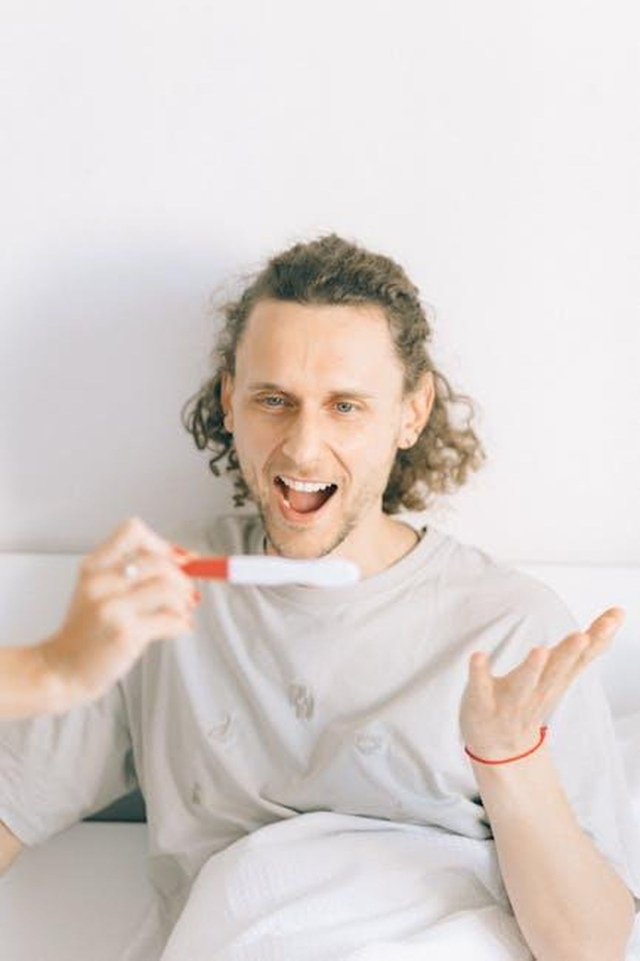 Rumori_di_separazione_D65KLrXA7O - Confidenze24 Source: Nataliya Vaitkevich - pexels - A joyful man expressing excitement while holding a positive pregnancy test in a cozy home setting.