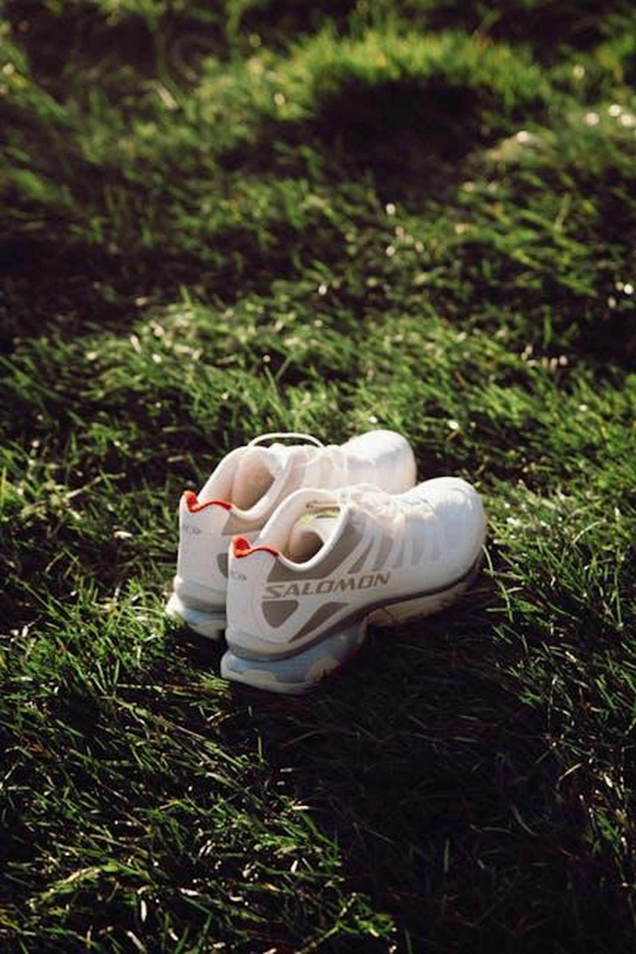 Salomon_e_la_sua_linea_di_sneakers_GOWGwdP5Rz - Confidenze24 Source: Nikola Vu - pexels - Pair of white Salomon running shoes resting on vibrant green grass under soft sunset light.