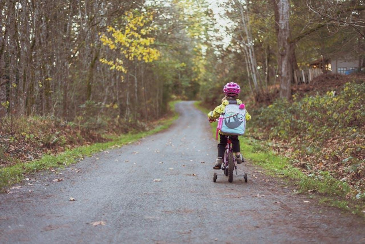 Sandy_Hook_Promise_un_impegno_per_la_sicurezza_dei_bambini_x2xKnJfdel - Confidenze24 Source: Vlad Vasnetsov - pexels - A young girl riding a bike with training wheels on a rural path surrounded by fall foliage.