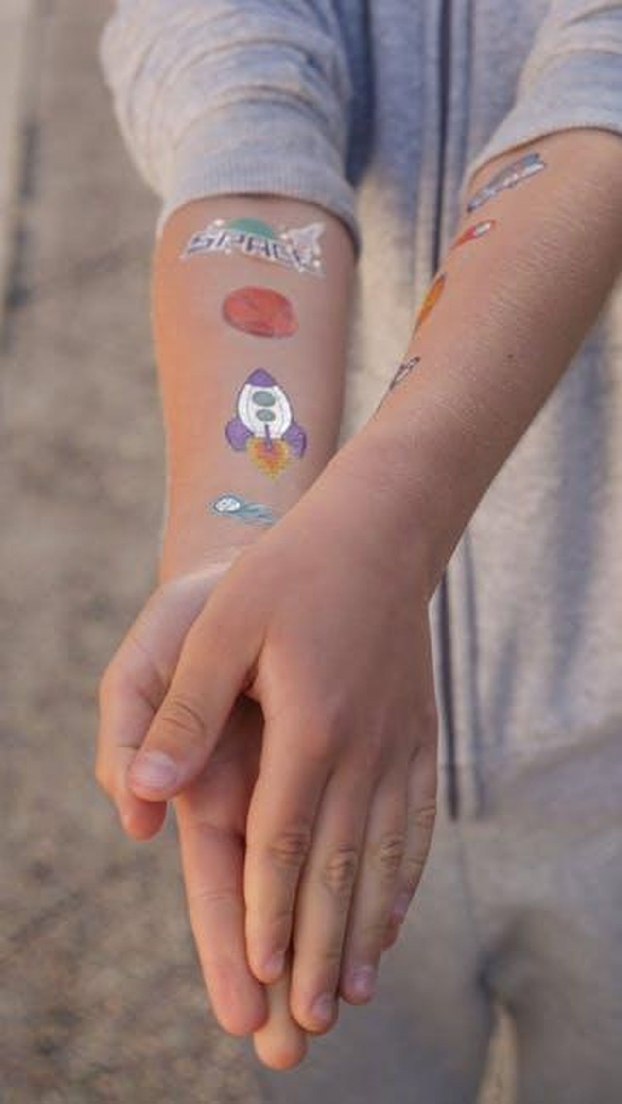 Scherzi_con_i_tatuaggi_o0MSvcytU1 - Confidenze24 Source: Kindel Media - pexels - Close-up of a child's arm covered with colorful space-themed temporary tattoos, including rockets and planets.