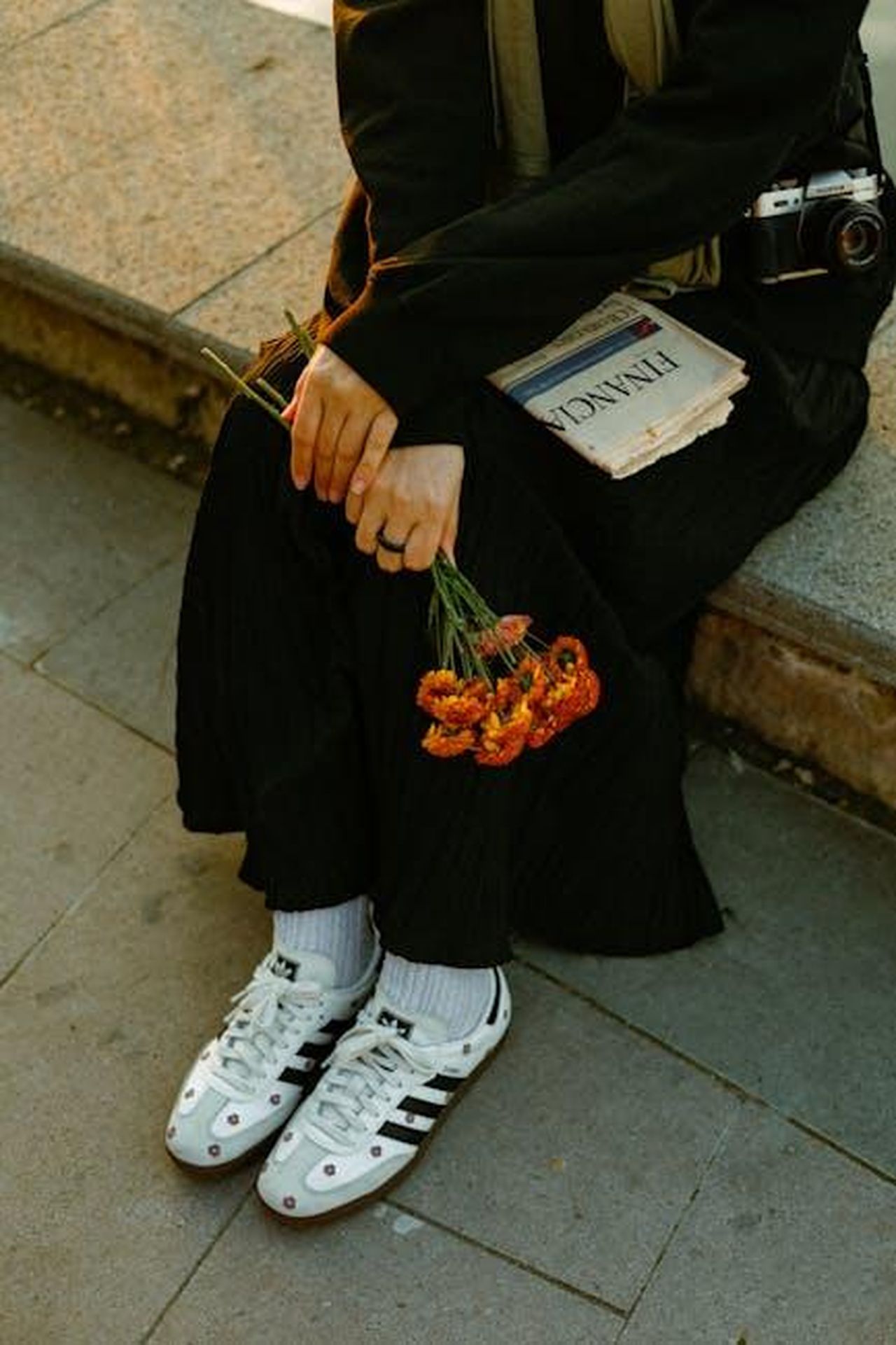 Scorpione_23_ottobre__21_novembre_qxye1zW2QF - Confidenze24 Source: Esra Korkmaz - pexels - A person sits on a bench holding flowers and a newspaper, wearing casual attire.