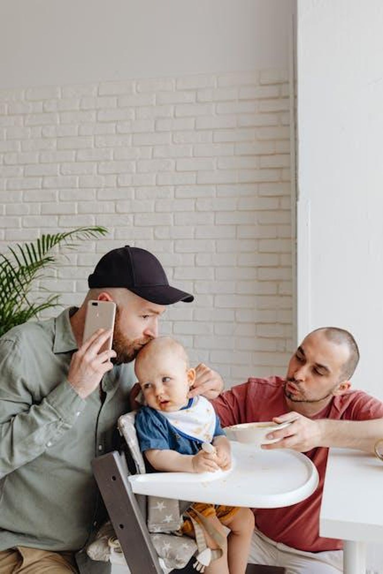 Shemar_Moore_e_Jesiree_Dizon_una_cogenitorialit_positiva_9VQXhHJK4f - Confidenze24 Source: Photo By: Kaboompics.com - pexels - Two fathers with a baby in a high chair, sharing a caring moment in a bright kitchen.