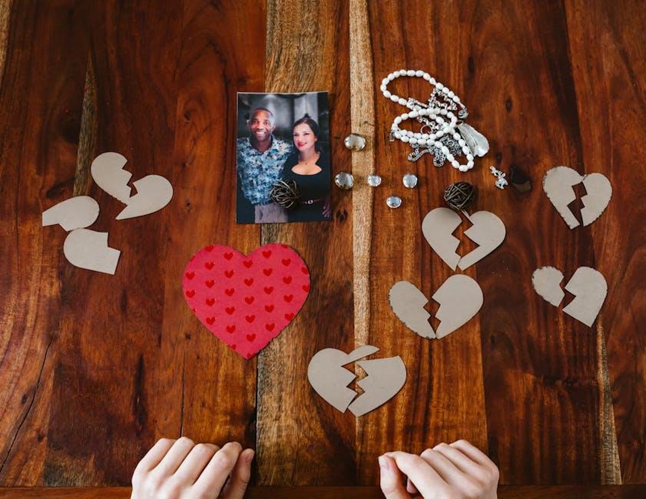 Shobna_parla_delle_relazioni_passate_Wah4C2csTU - Confidenze24 Source: RDNE Stock project - pexels - A collection of broken heart symbols, jewelry, and a couple's photo on a wooden surface.