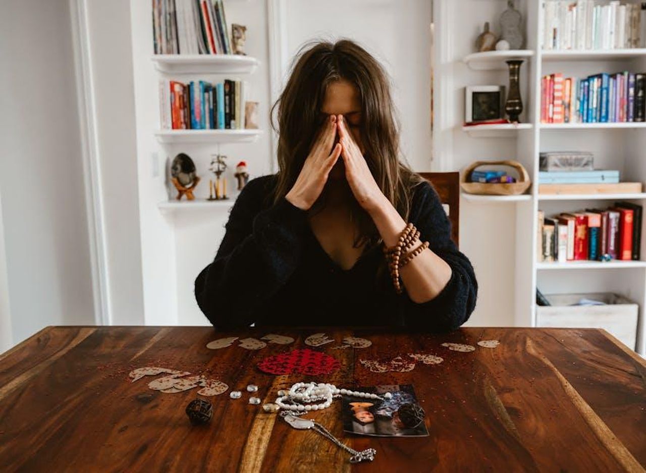 Situazione_di_vita_estraniata_ygzEDpY4g4 - Confidenze24 Source: RDNE Stock project - pexels - A woman in deep thought sits at a table with beads and a photo, conveying introspection.
