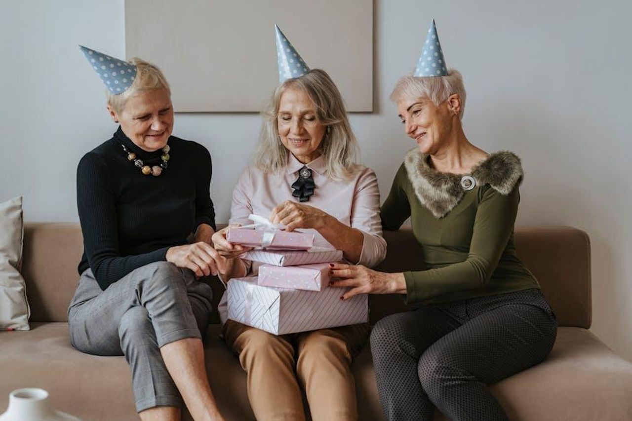 Tamar_Celebra_il_Suo_Compleanno_AcetIltlyu - Confidenze24 Source: olia danilevich - pexels - Three senior women celebrating a birthday with gifts and party hats indoors.